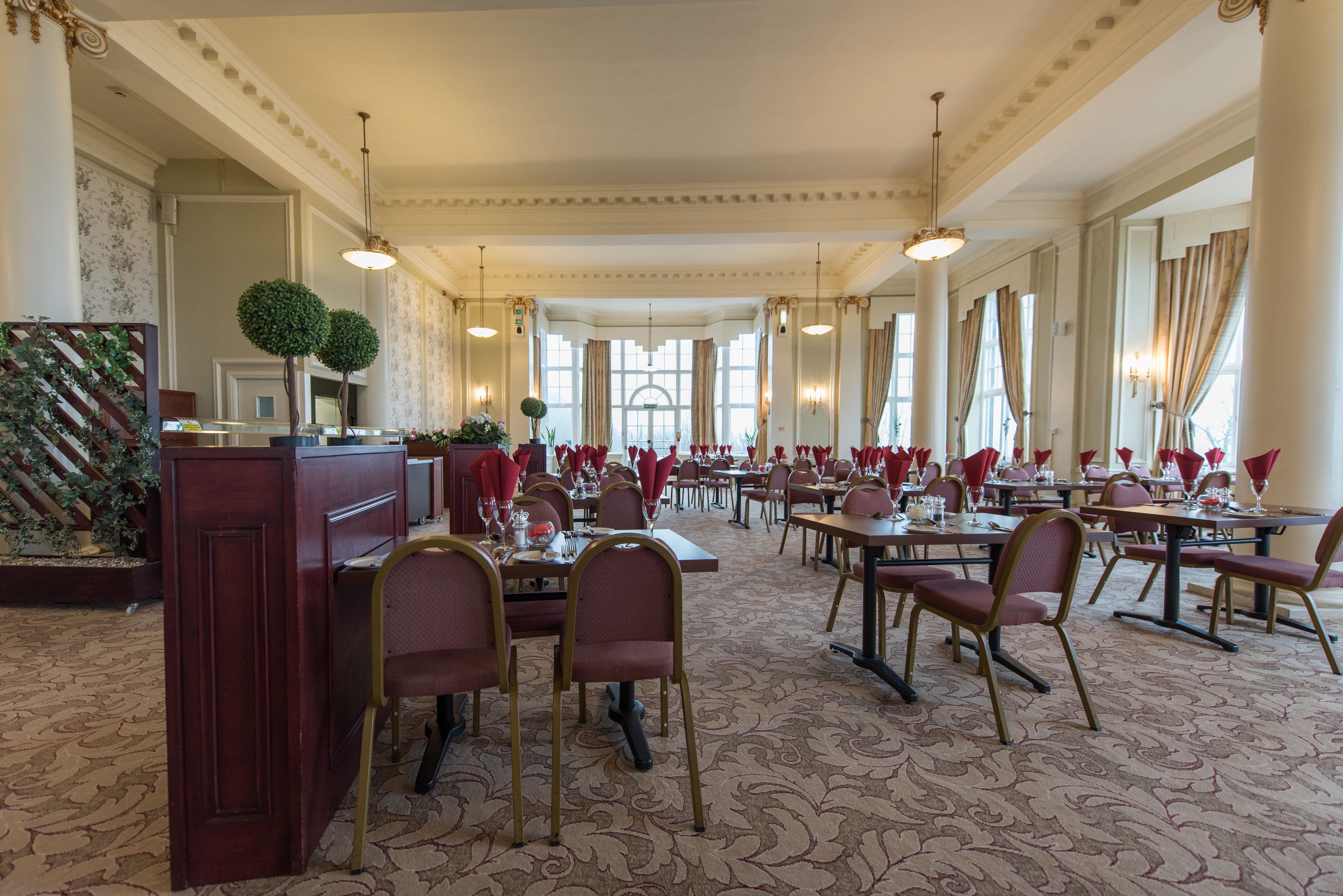 A spacious banquet hall with multiple tables and chairs, large windows, and a classic architectural design.