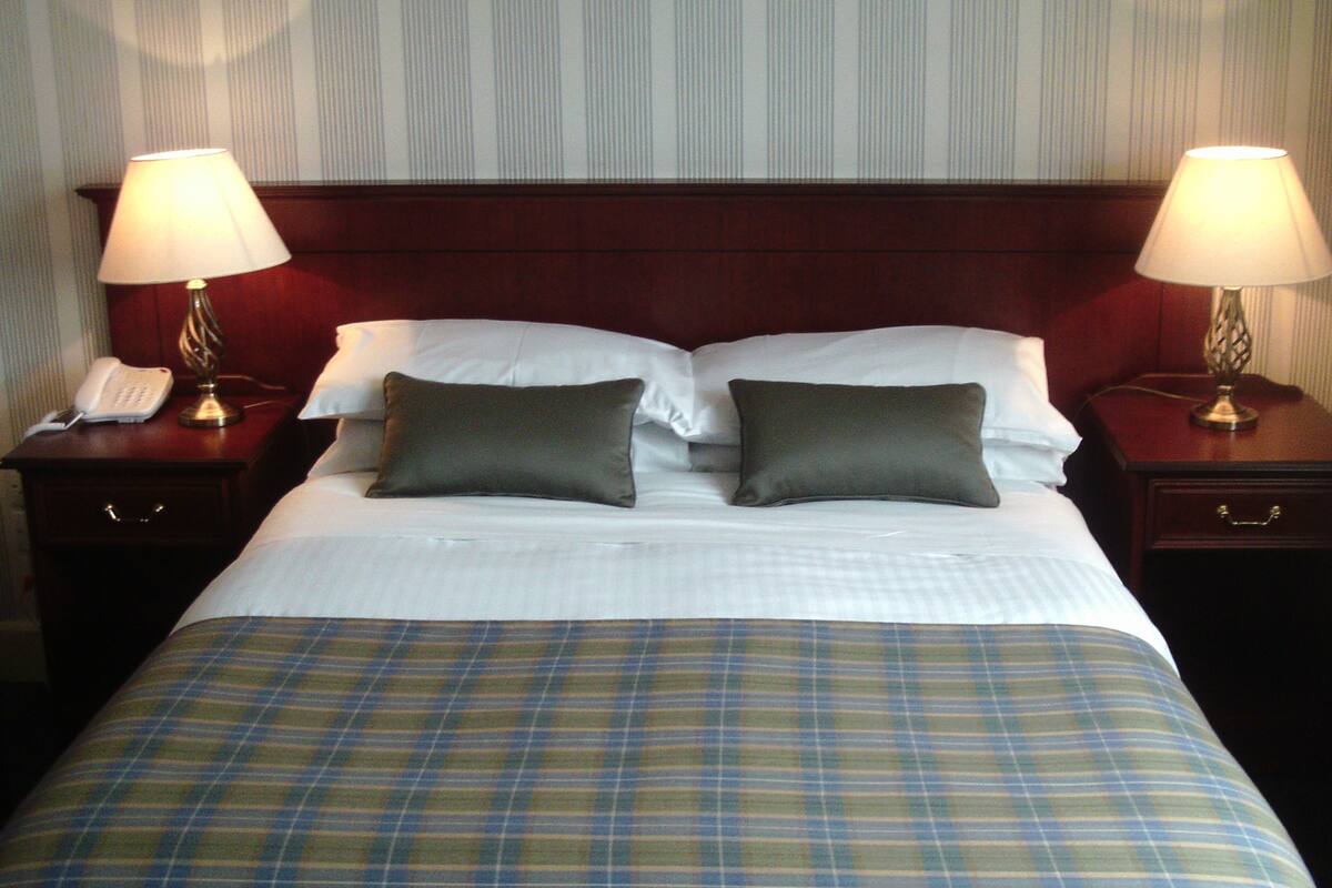 A hotel room with a bed, two bedside tables with lamps, a telephone, and a plaid bedspread.