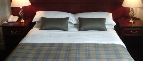 Una habitación de hotel con una cama, dos mesitas de noche con lámparas, un teléfono y una colcha a cuadros.