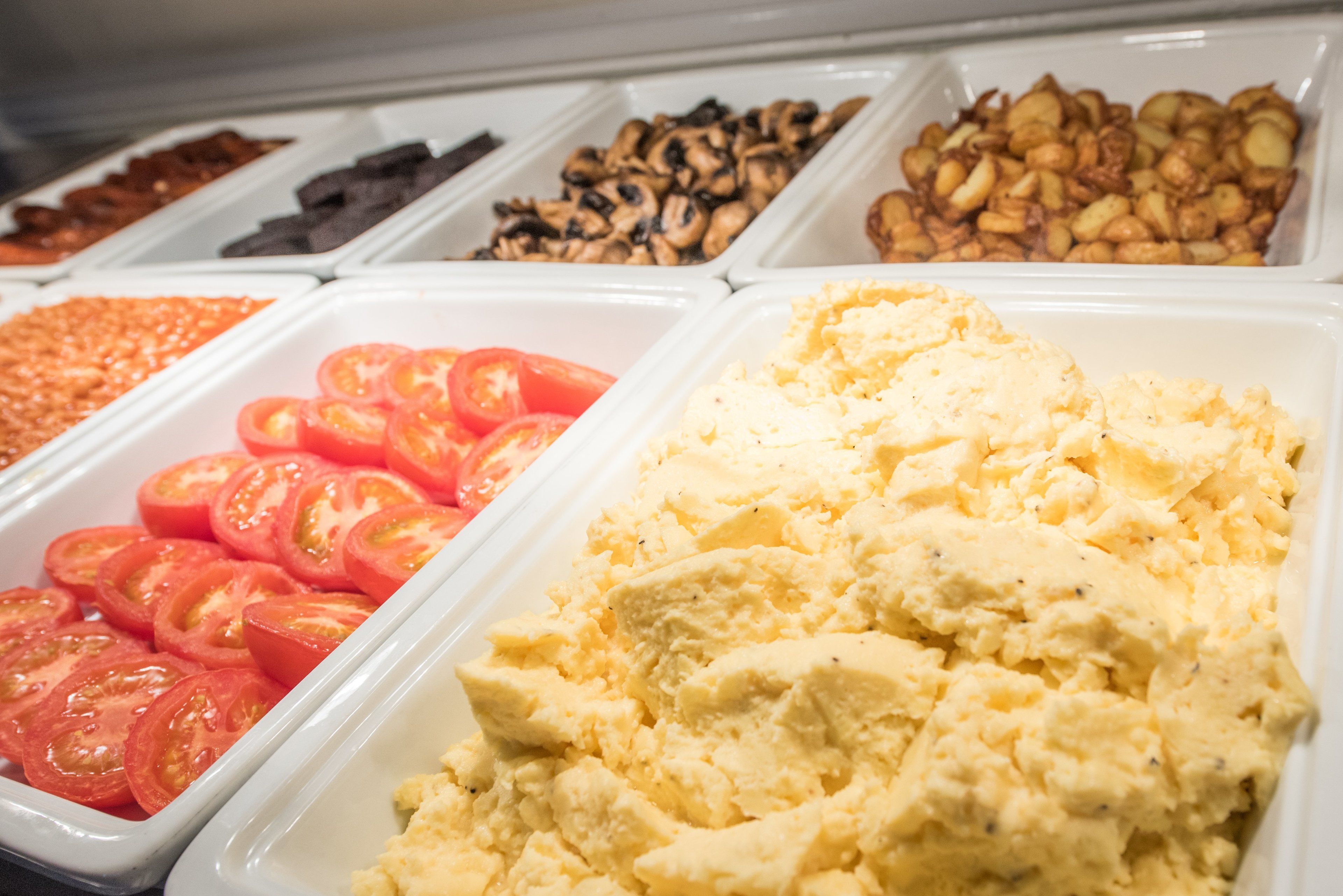 A buffet with various food items including sliced tomatoes, scrambled eggs, and different types of nuts.