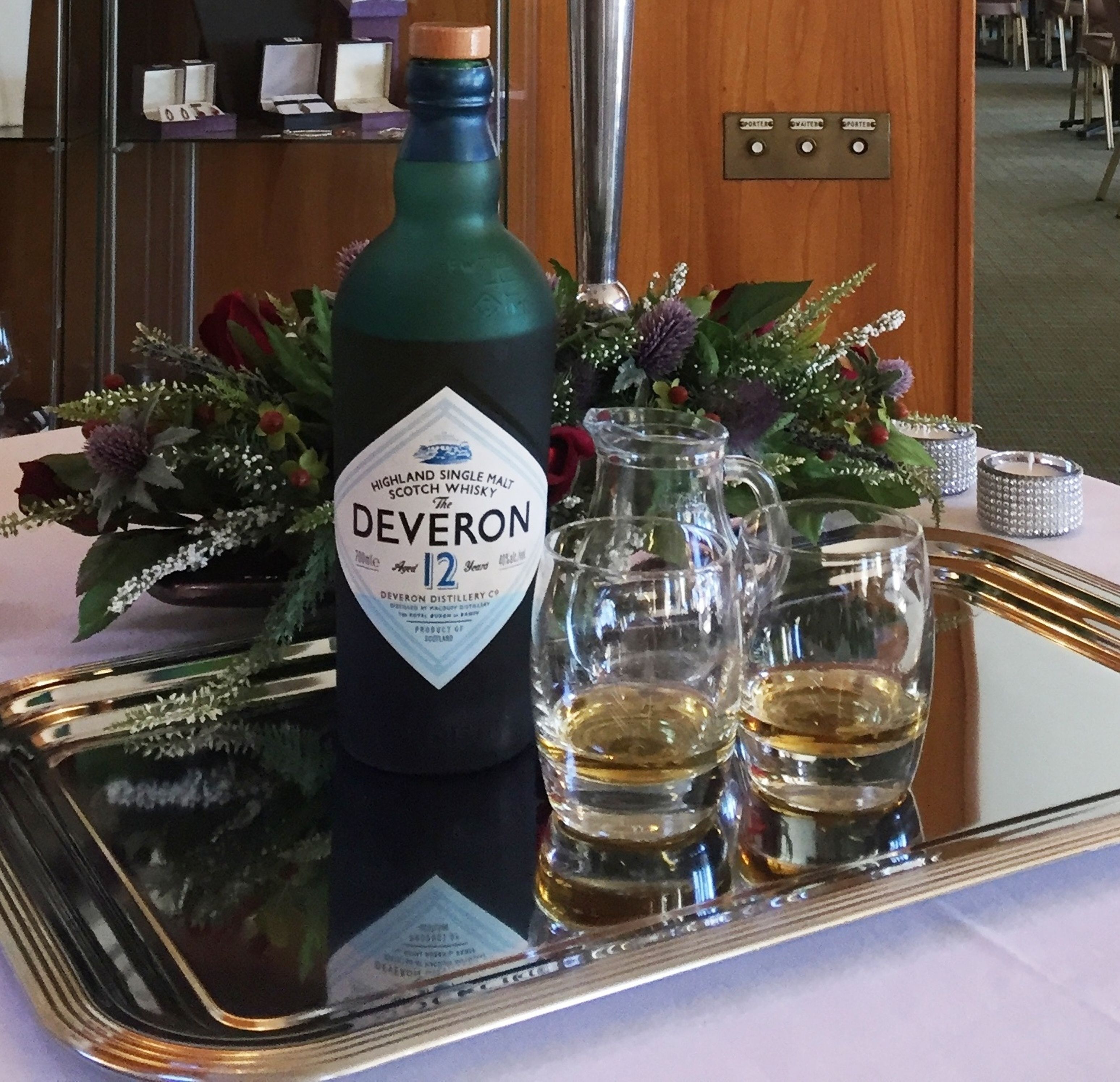 A bottle of Highland Single Malt Scotch Whisky, The Deveron 12, on a tray with two glasses of whisky.