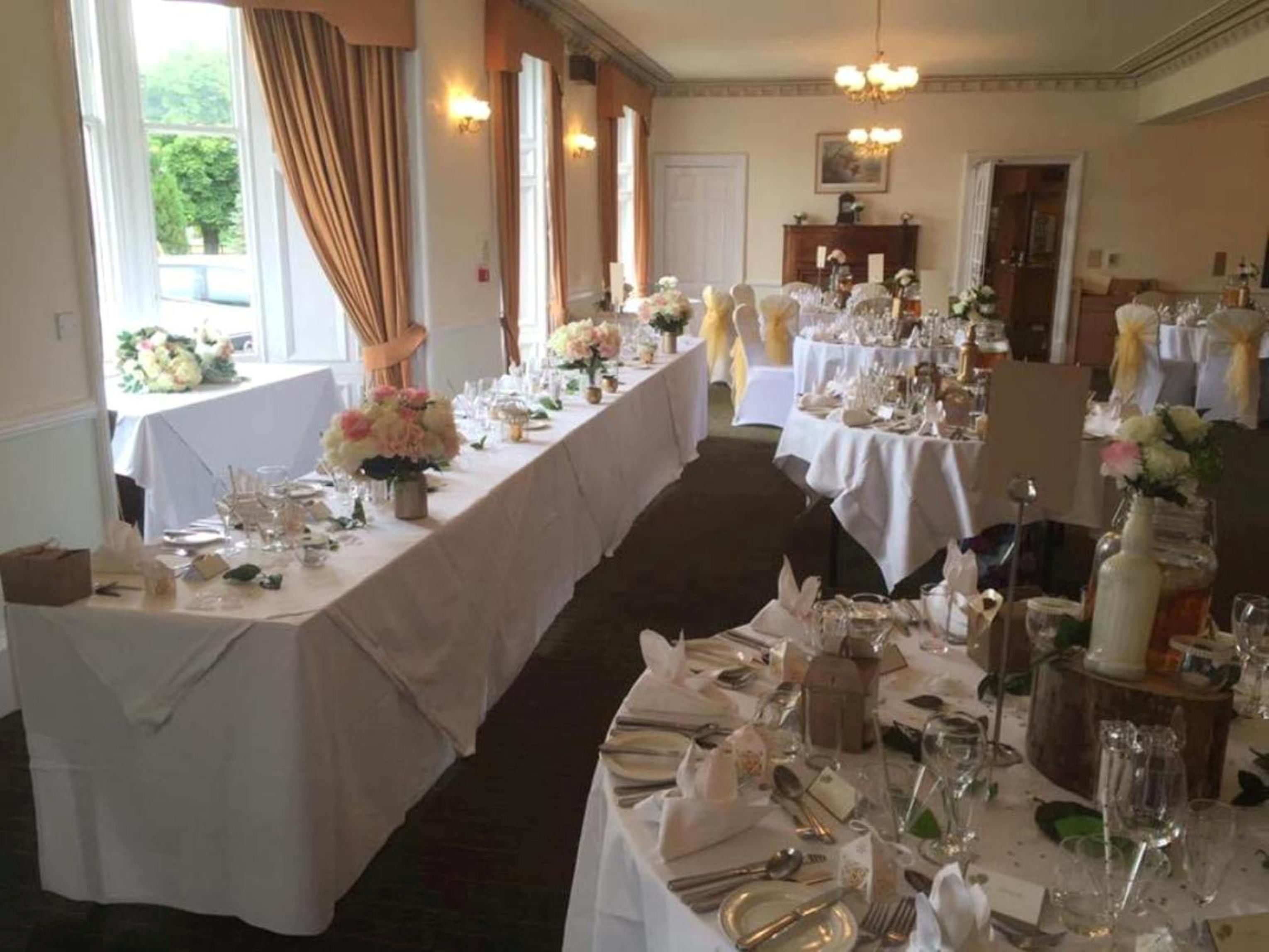 A banquet hall with long tables set for a formal event, featuring white tablecloths and floral centerpieces.