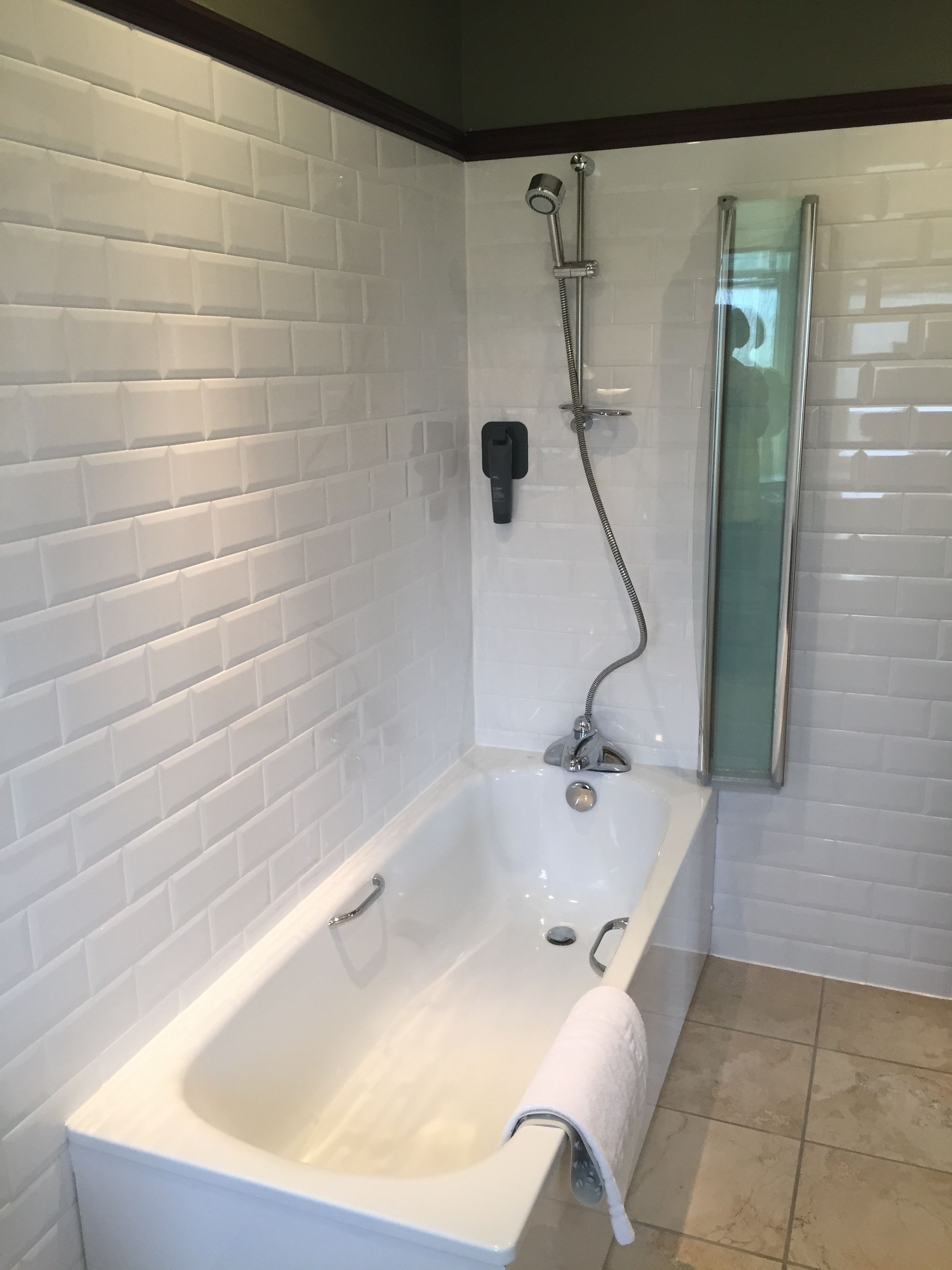 A modern bathroom with white subway tiles, a white bathtub, and a glass shower enclosure.