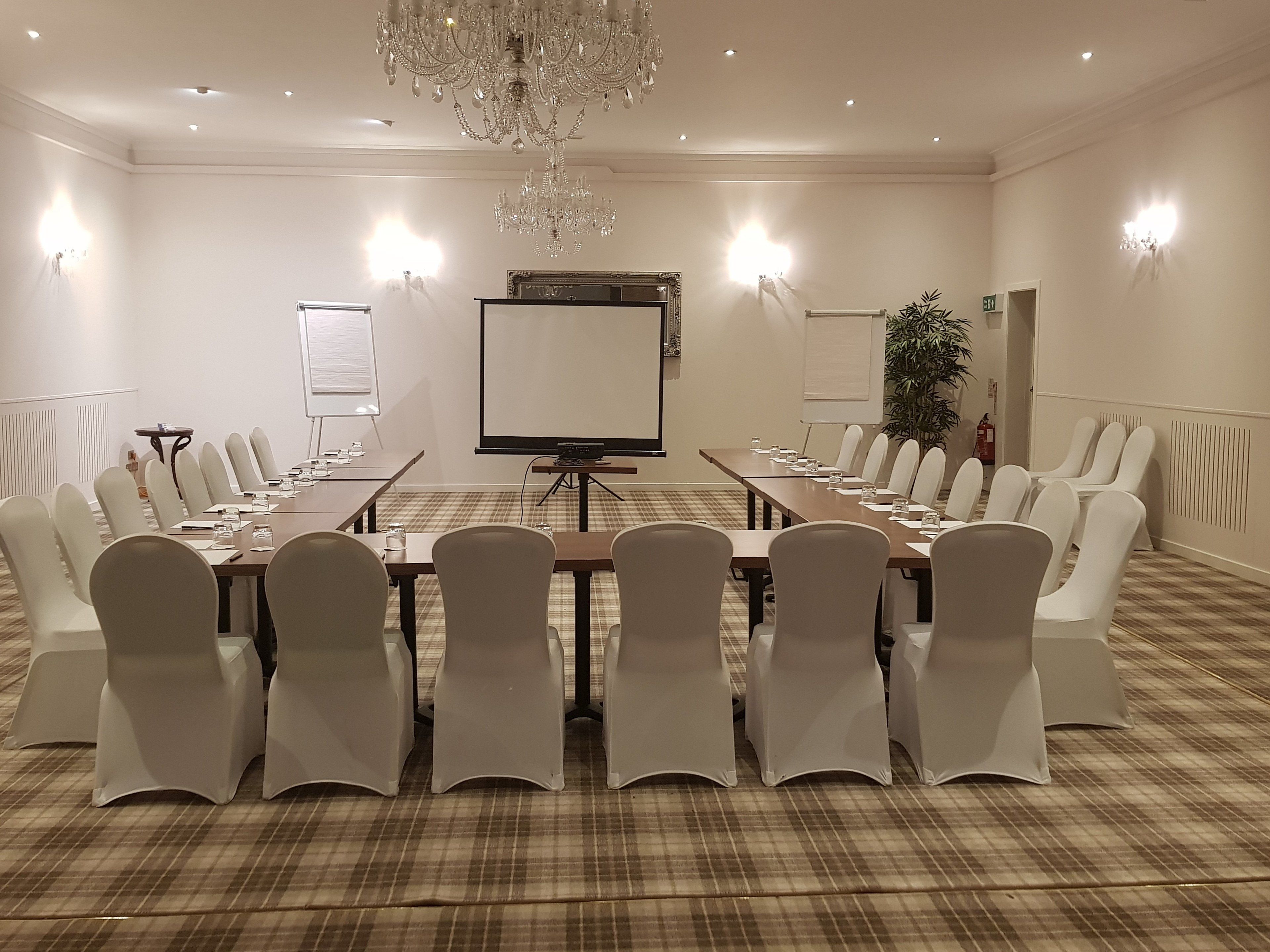 A conference room with a long table, white chairs, a projector screen, and a chandelier.
