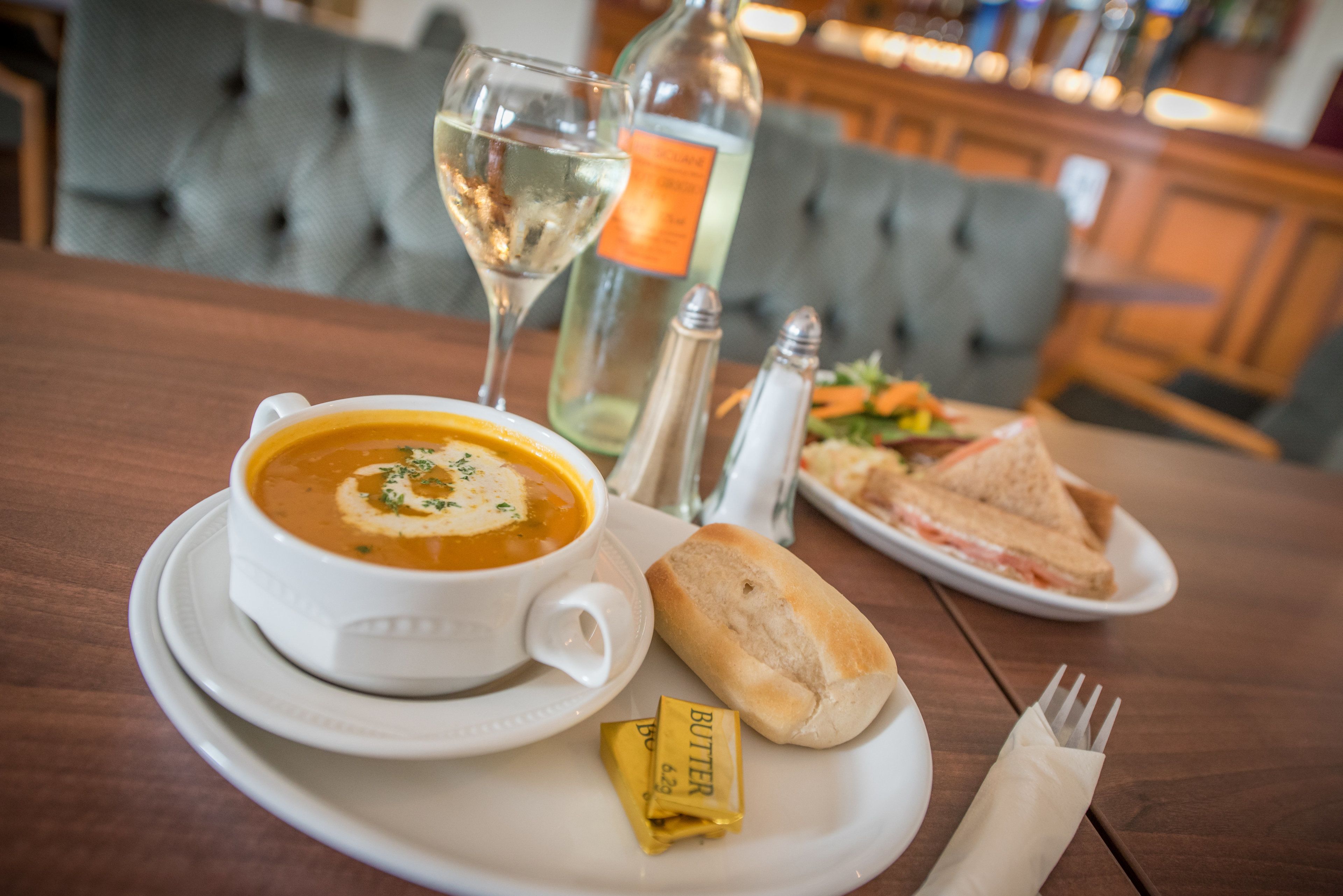 A dining table with a bowl of soup, a sandwich, a bottle of wine, and condiments.