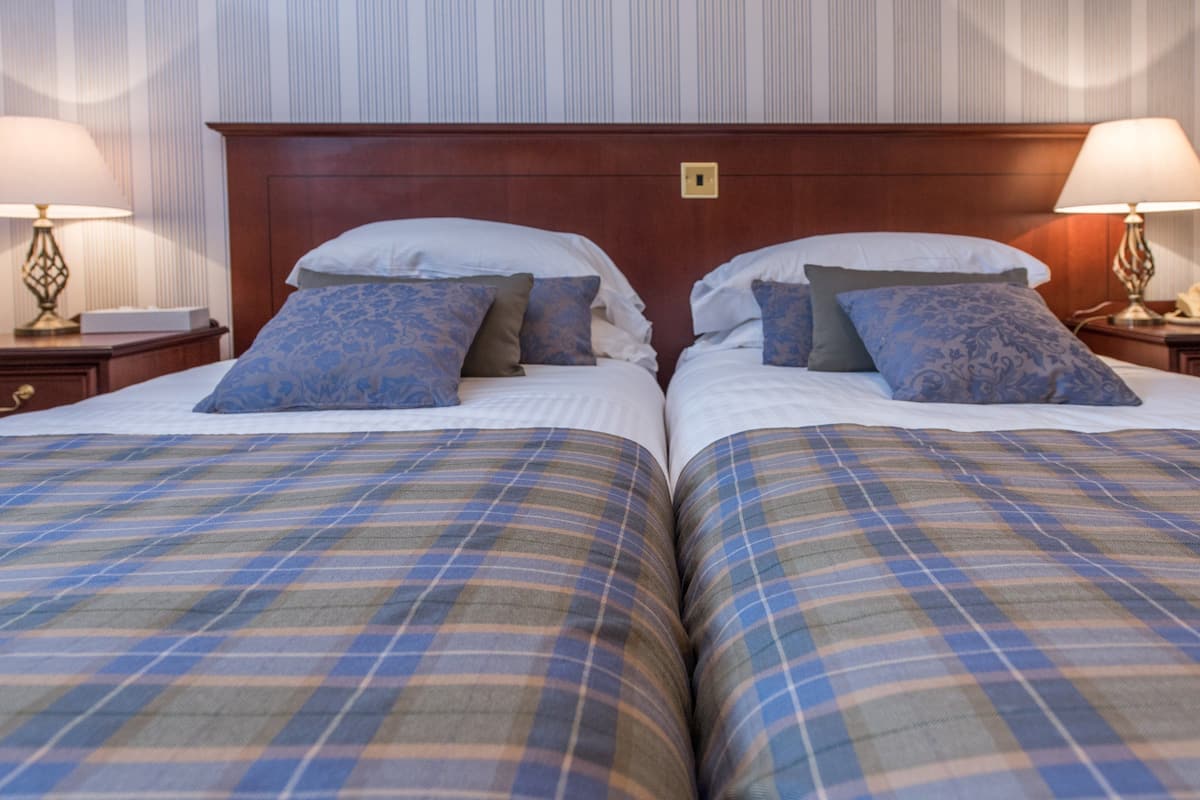 A double bed with plaid bedding and two pillows, a wooden headboard, and bedside lamps.