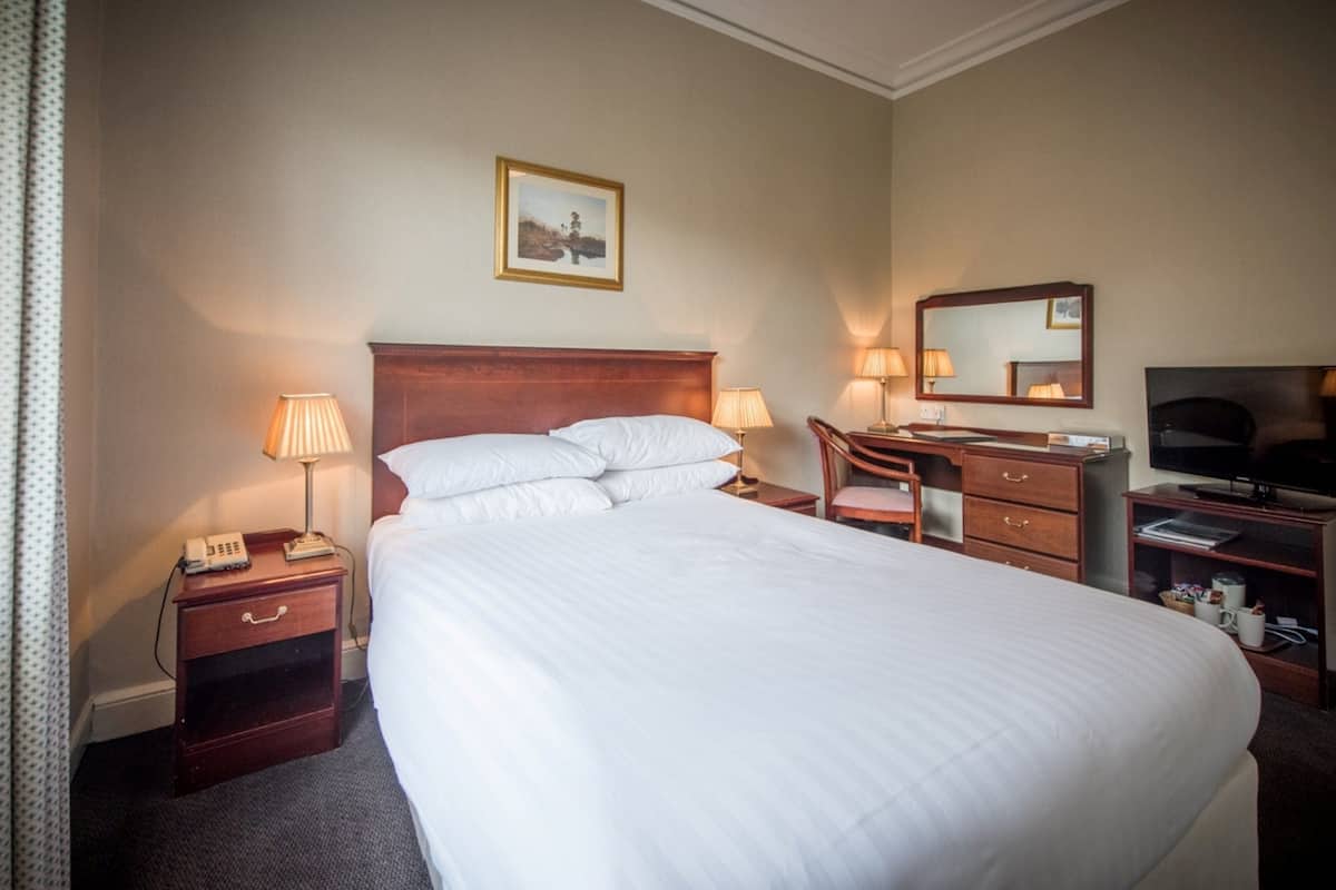 A hotel room with a large bed, bedside lamps, a desk with a chair, a television, and a mirror.