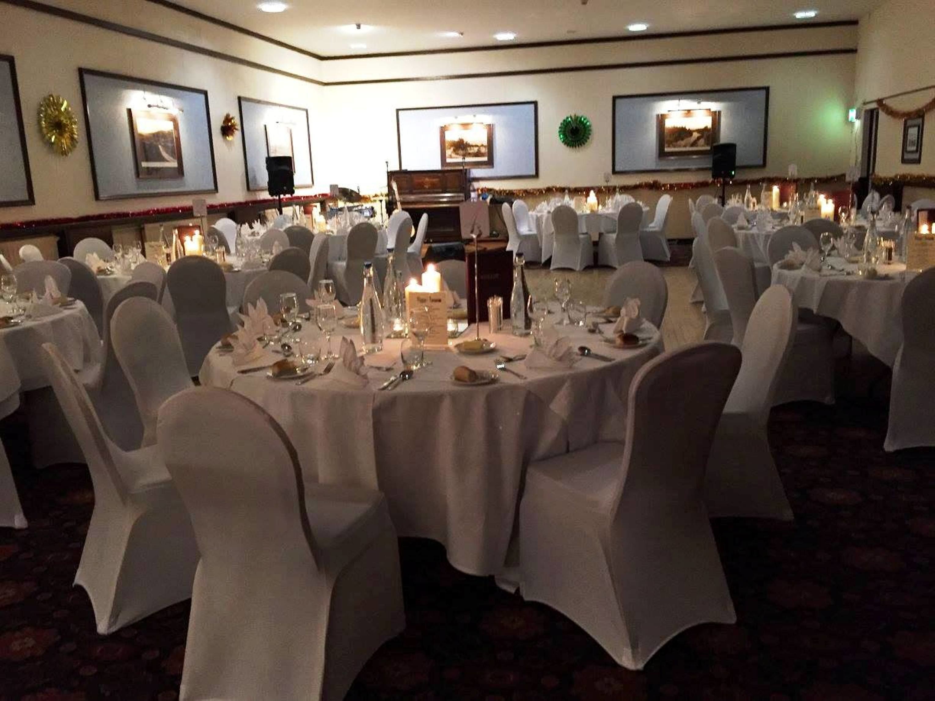 A banquet hall with round tables set for a formal event, featuring white tablecloths and chairs.
