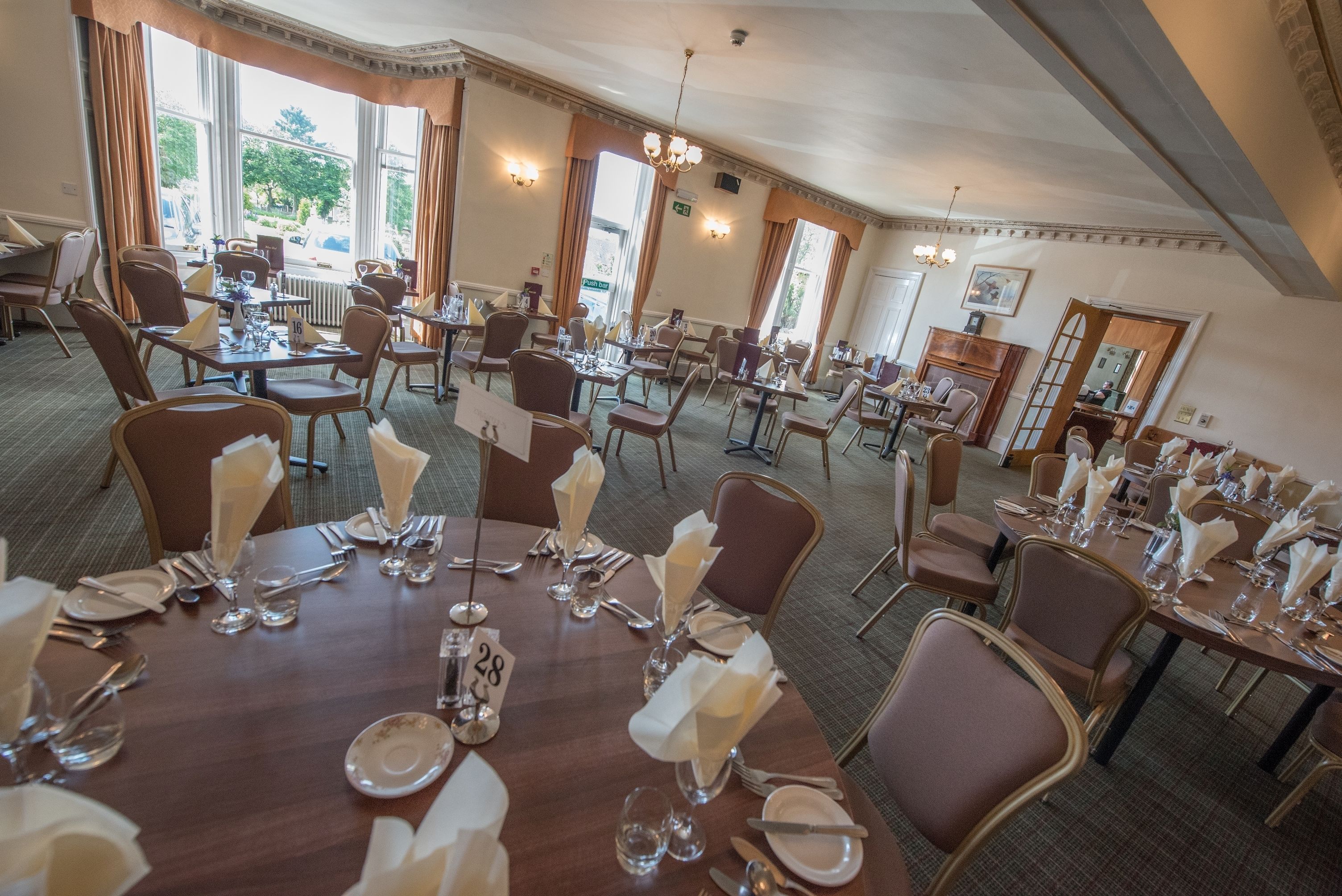 A spacious dining area with multiple tables set for service, large windows offering a view of the outdoors, and classic interior design elements.