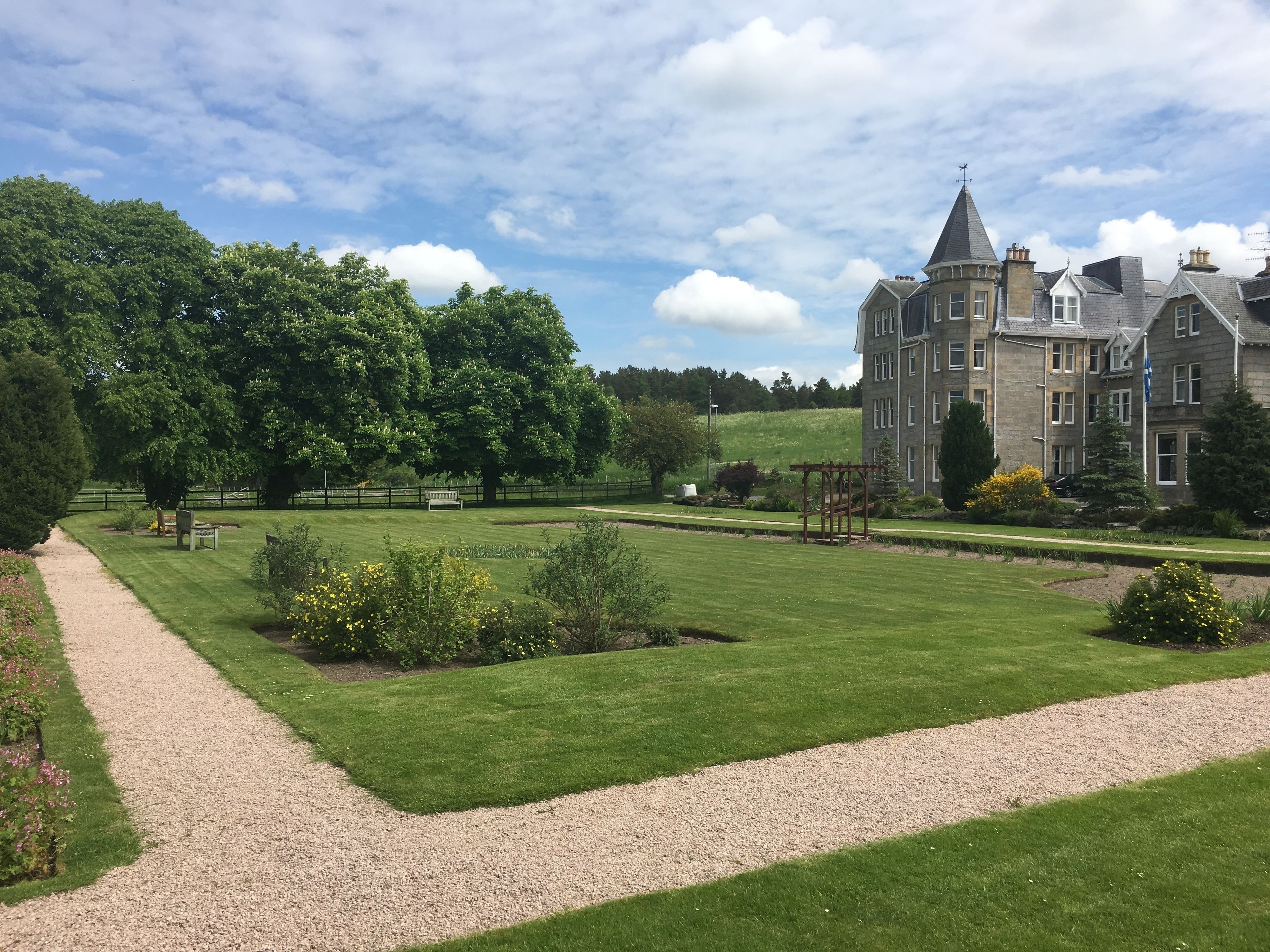 A large, historic building with a formal garden, a gravel path, and a well-maintained lawn.