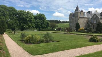 A large, historic building with a formal garden, a gravel path, and a well-maintained lawn.