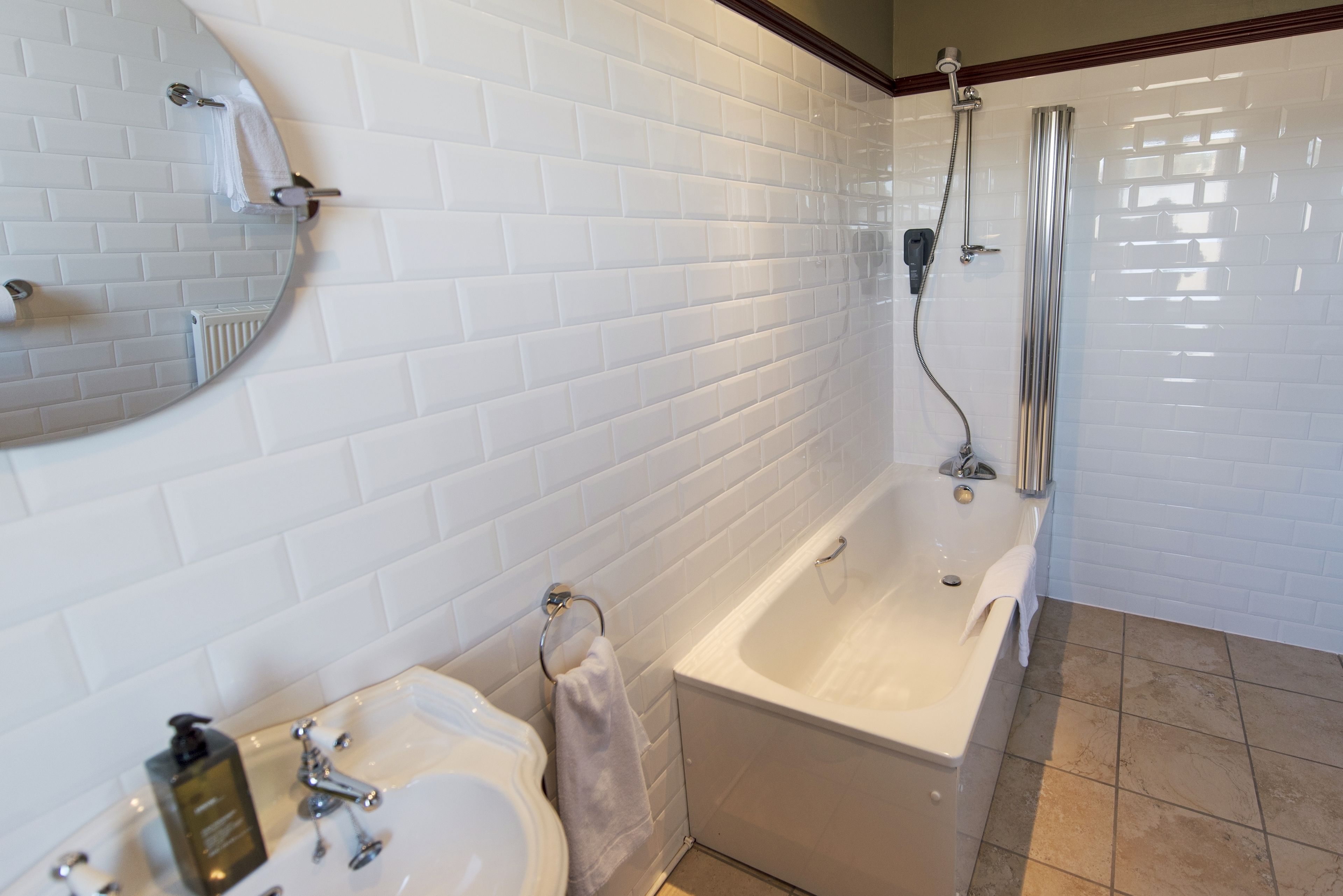 Une salle de bain avec des murs carrelés de blanc, une baignoire, un lavabo et un miroir.