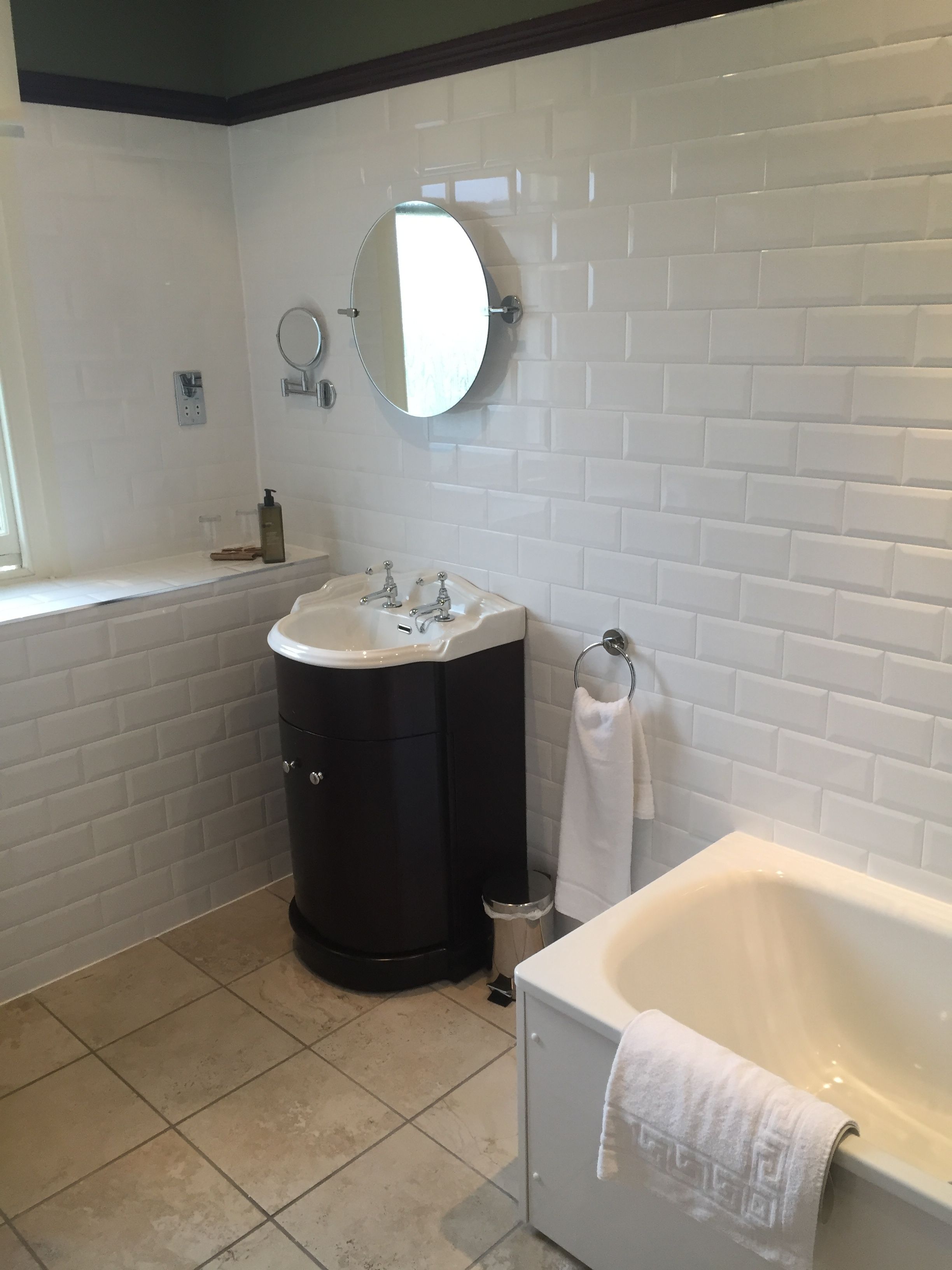 A bathroom with a white bathtub, a round mirror, a black vanity, and a tiled wall.