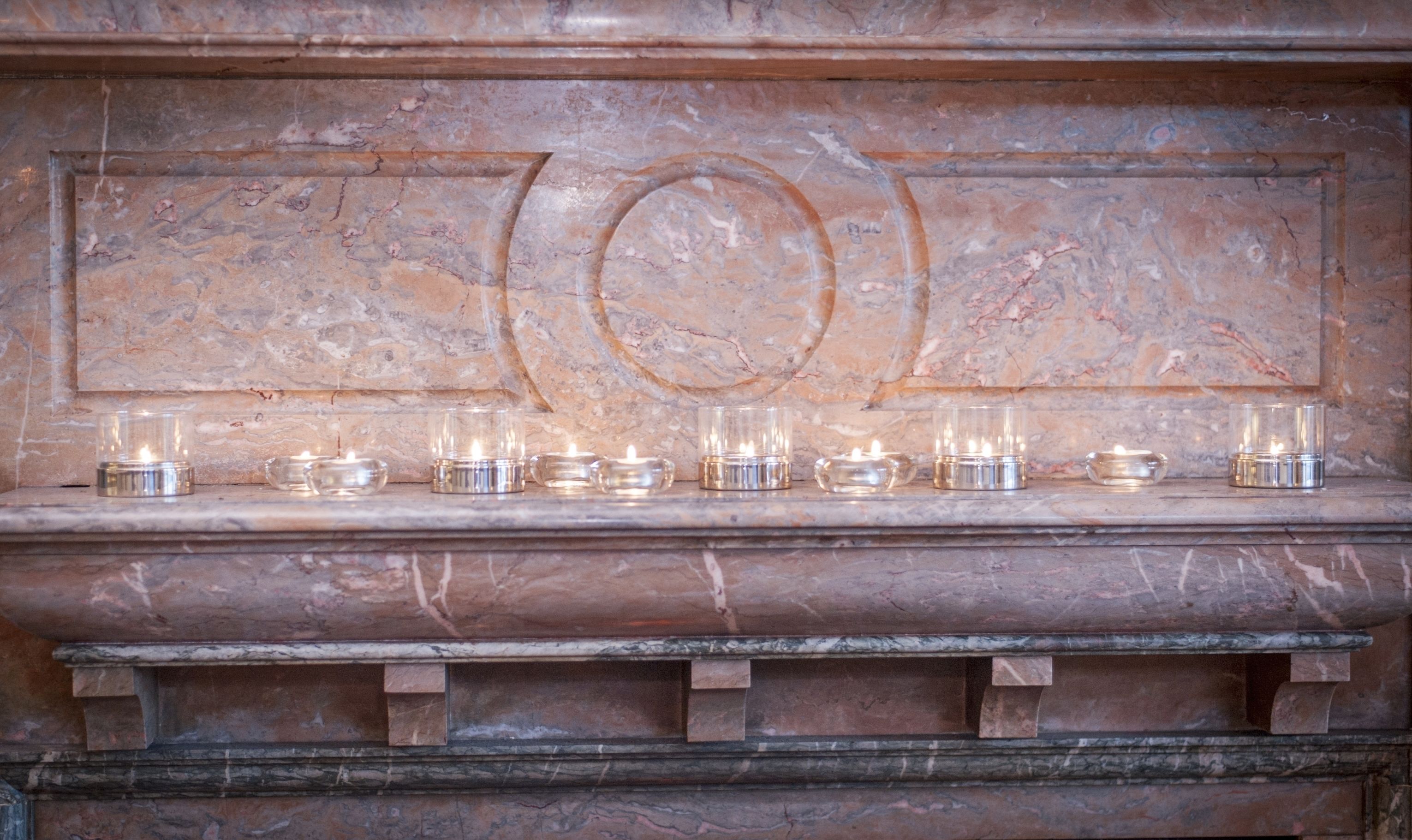 Une cheminée en marbre ornée d’un panneau décoratif et de nombreuses bougies allumées.