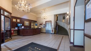 A hotel lobby with a reception desk, chandeliers, a staircase, and a doormat with the hotel name. - The Royal Hotel (Oban)