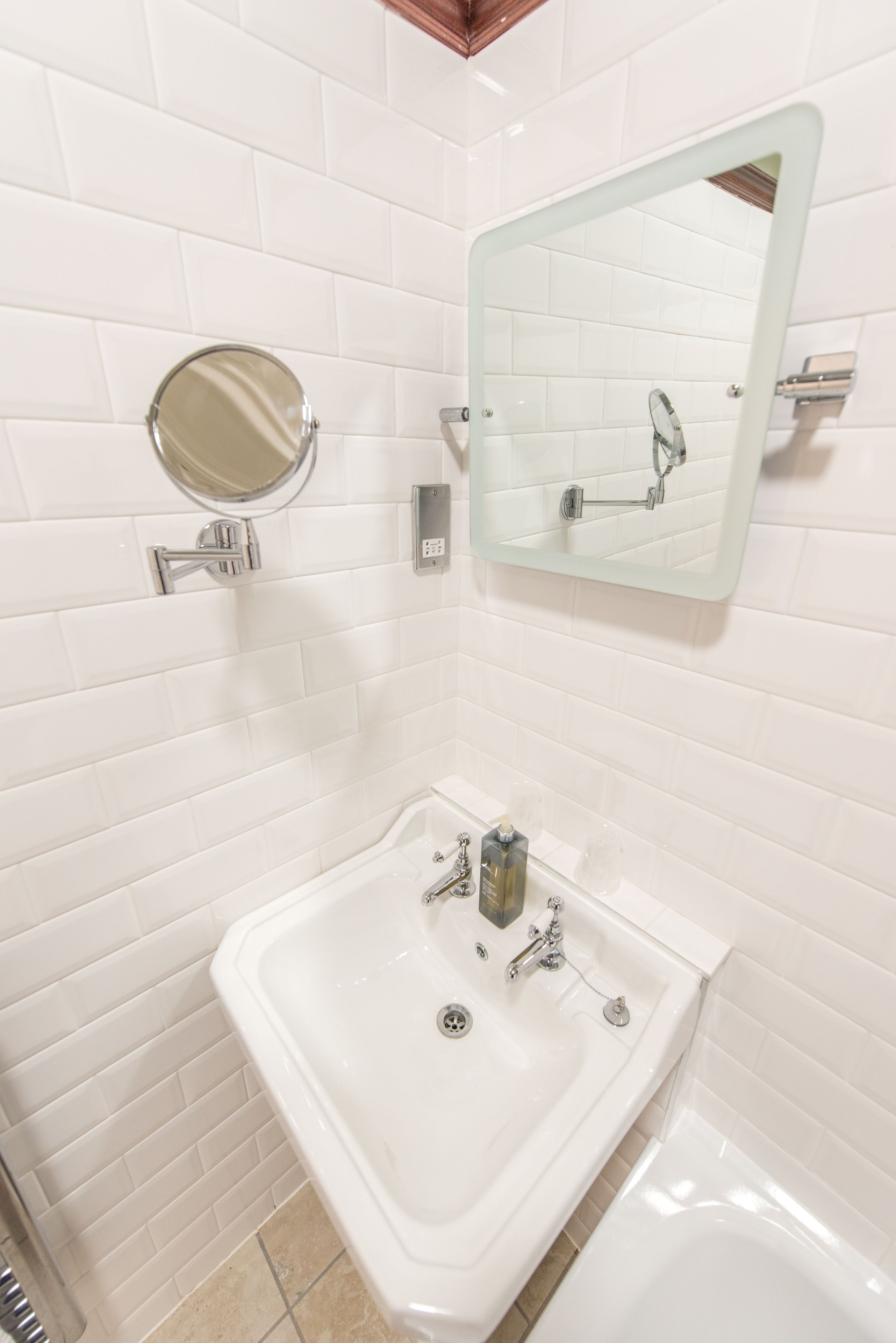 Een badkamer met witte betegelde wanden, een witte wastafel, een spiegel en een bad.