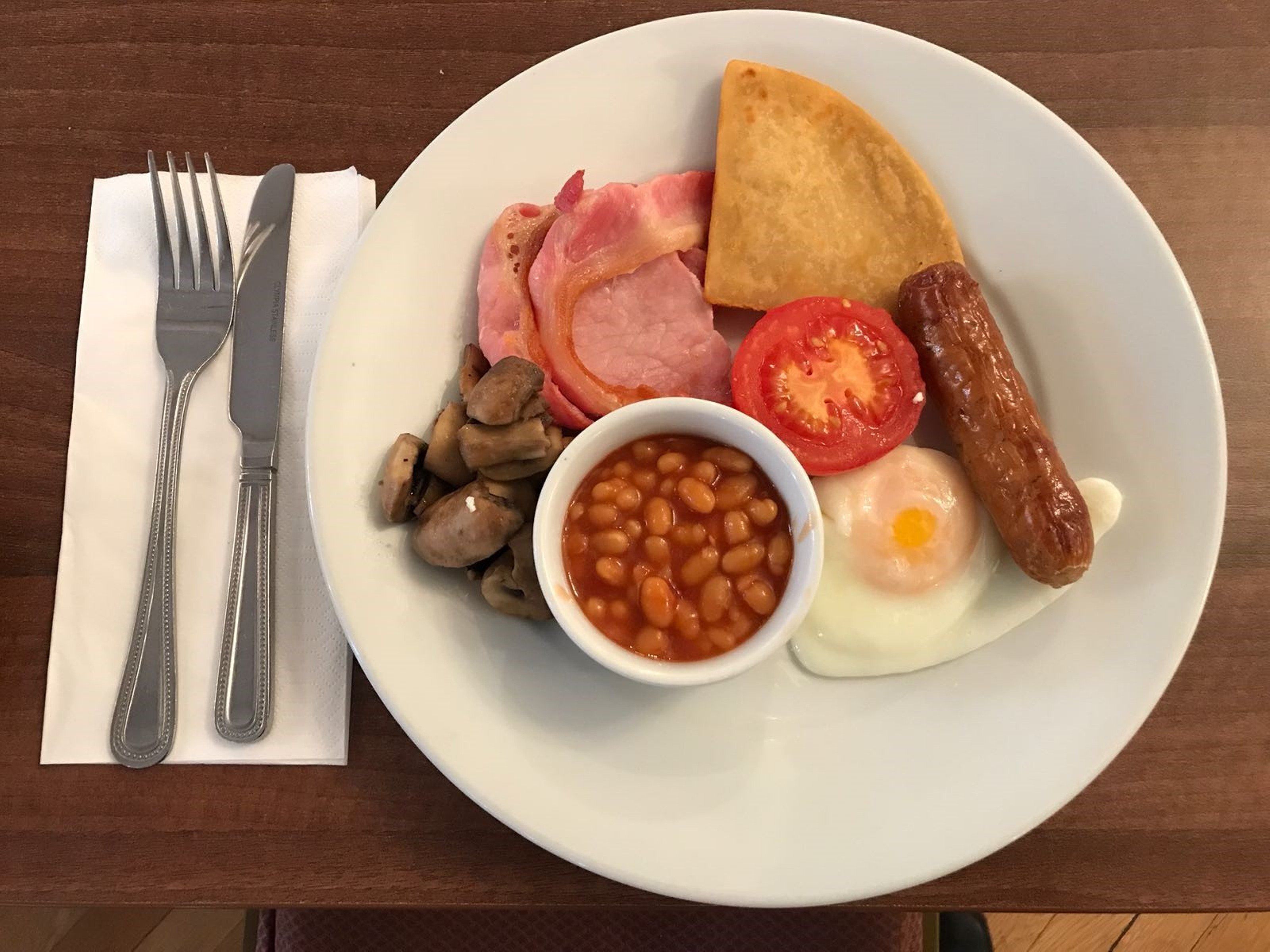 A plate of breakfast food including eggs, bacon, sausages, mushrooms, beans, tomatoes, and toast.
