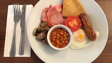 A plate of breakfast food including eggs, bacon, sausages, mushrooms, beans, tomatoes, and toast.