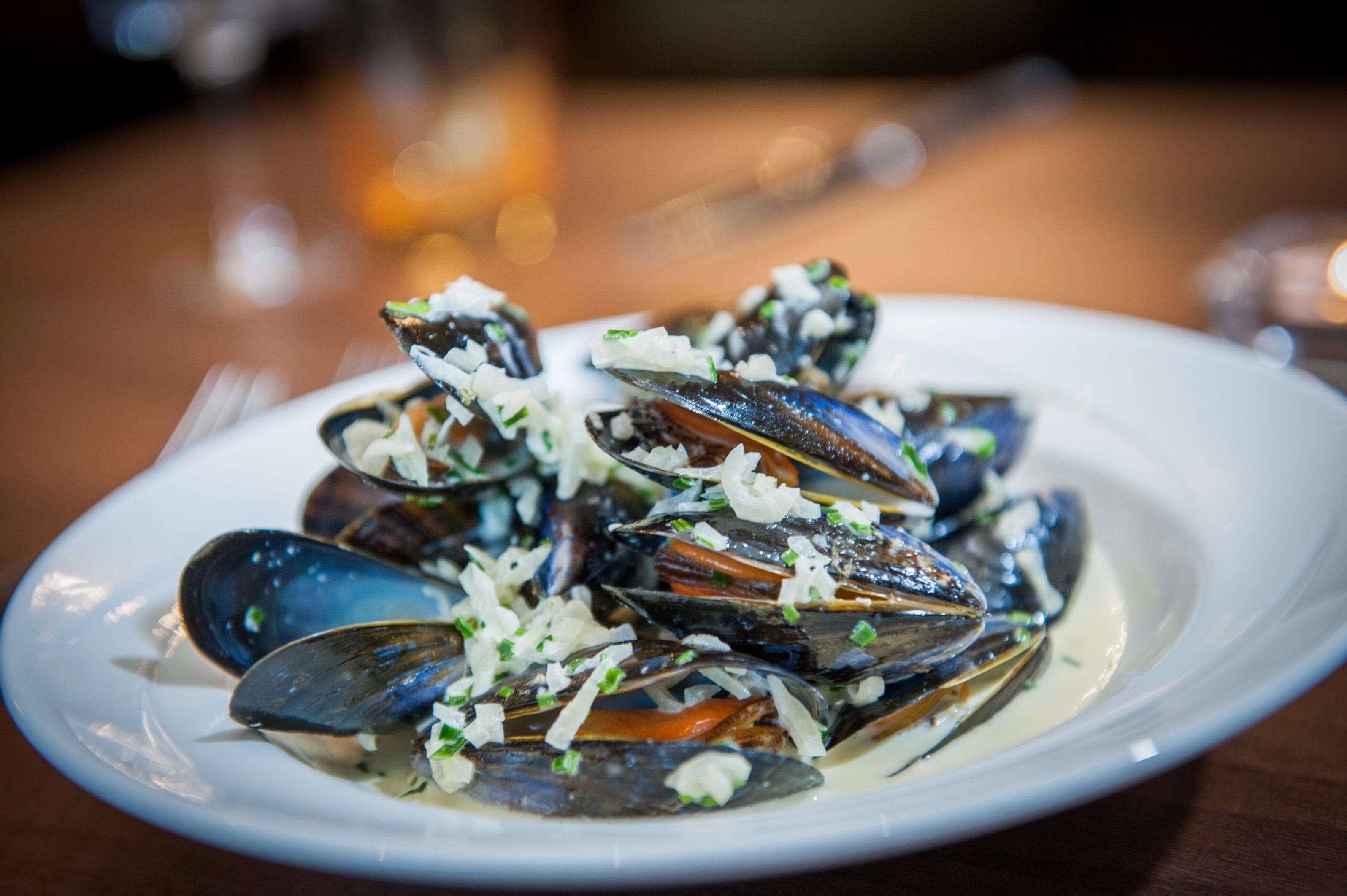 A plate of mussels with a creamy sauce and grated cheese.