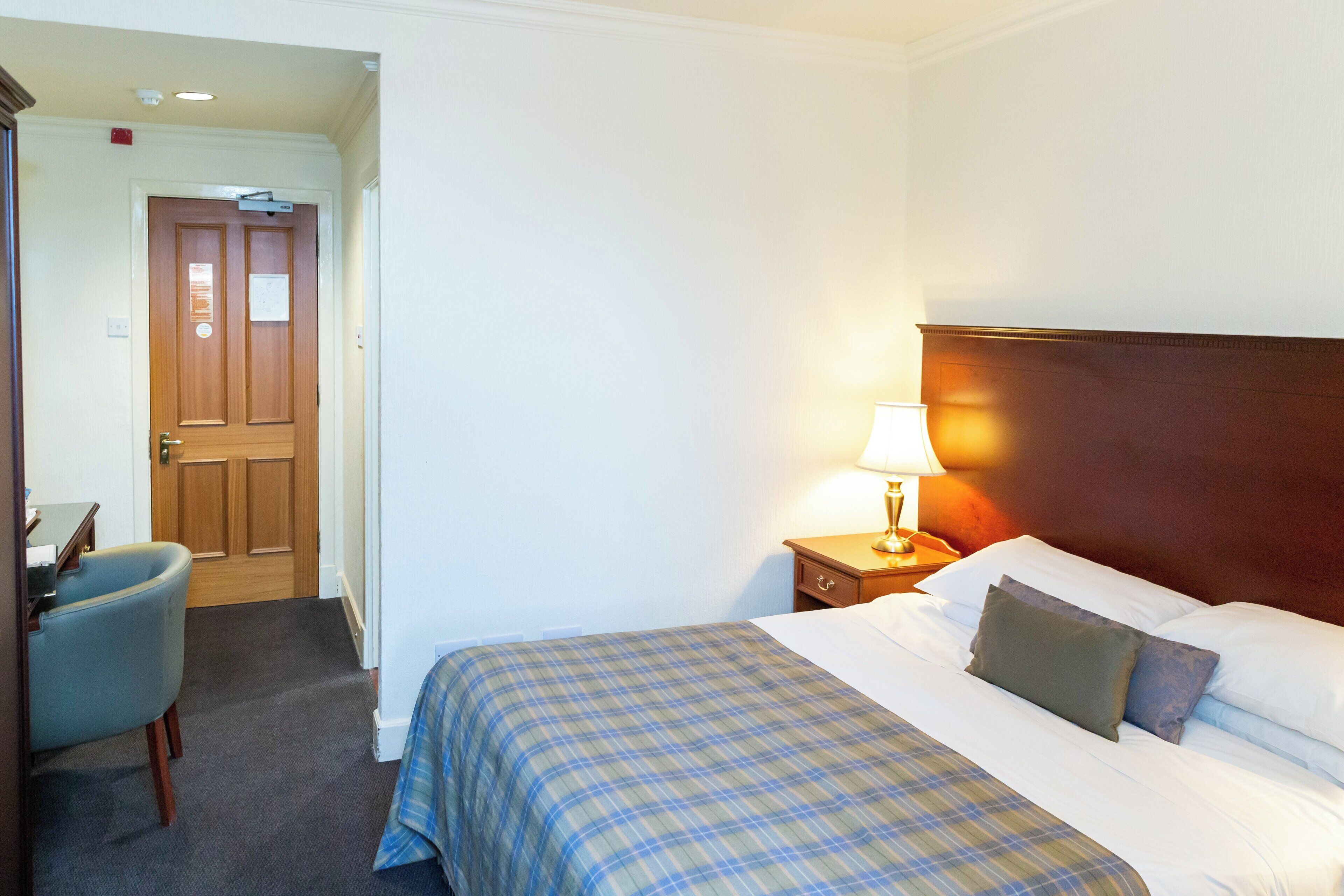 Une chambre d’hôtel avec un lit, une table de chevet avec une lampe, une chaise et une porte.