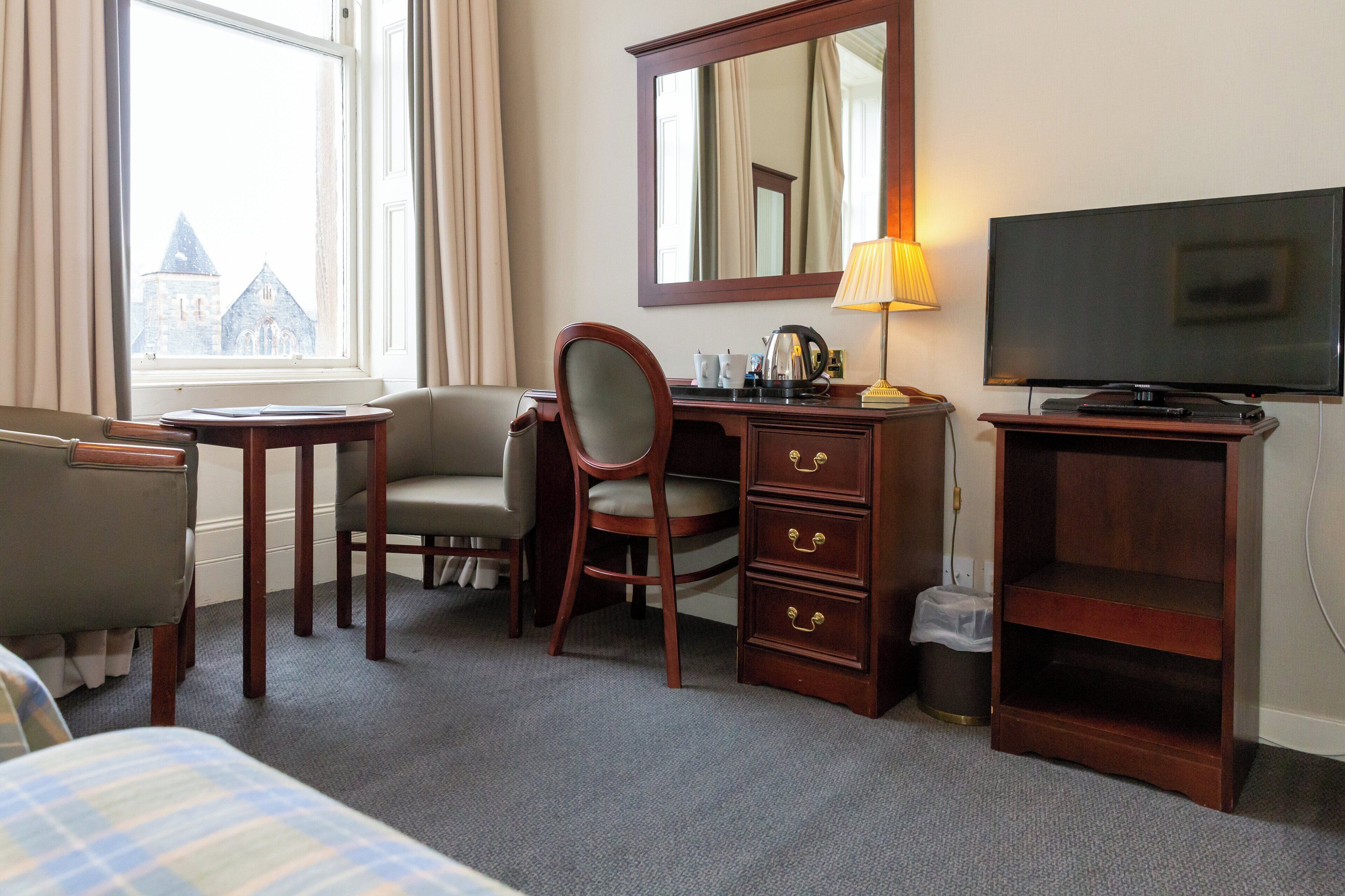 A hotel room with a bed, a desk, a chair, a television, and a dresser.