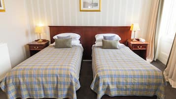 A hotel room with two beds, each with a plaid bedspread, wooden headboards, bedside tables with lamps, and a framed picture on the wall.
