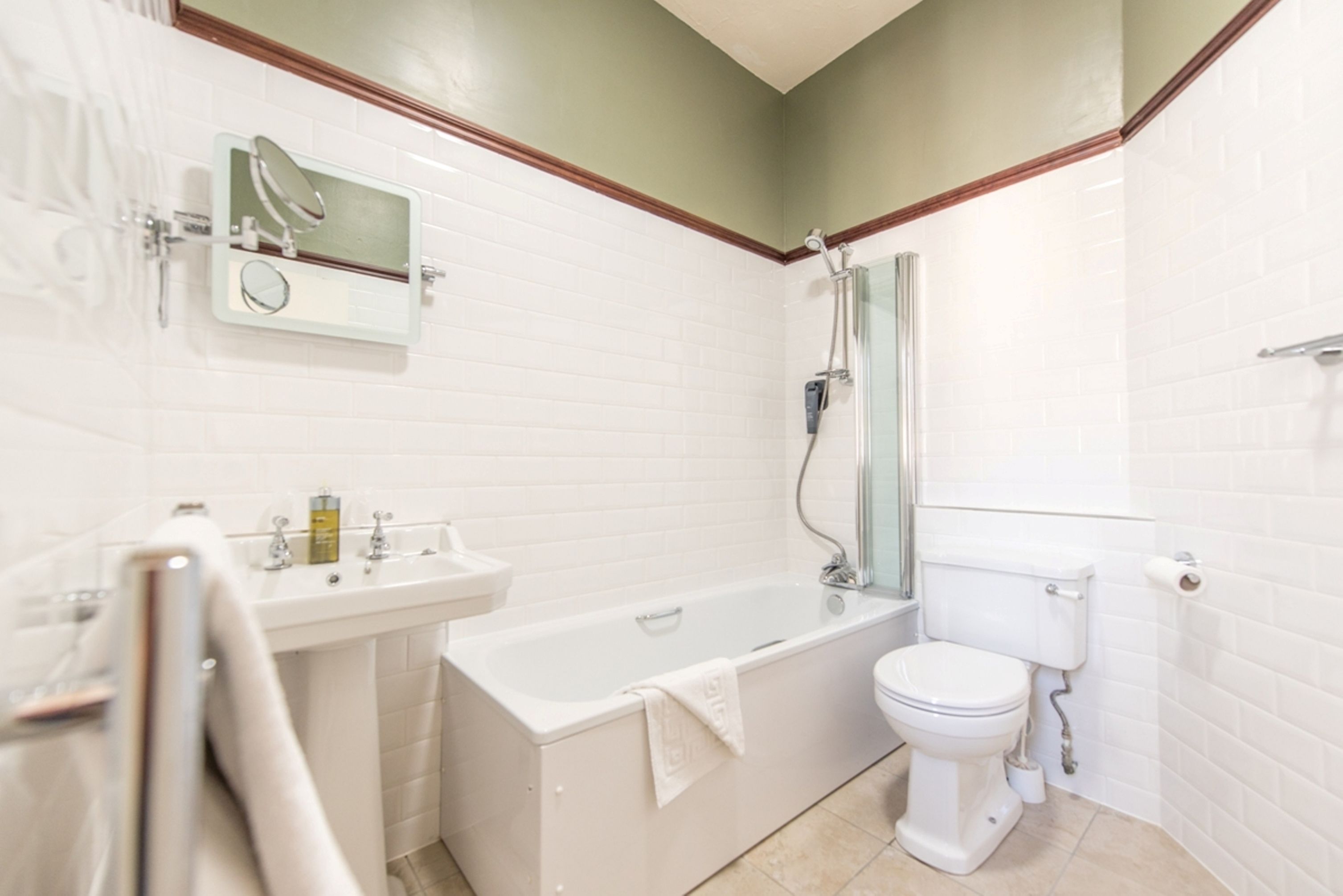 A bathroom with a bathtub, toilet, sink, and a mirror with a built-in light.