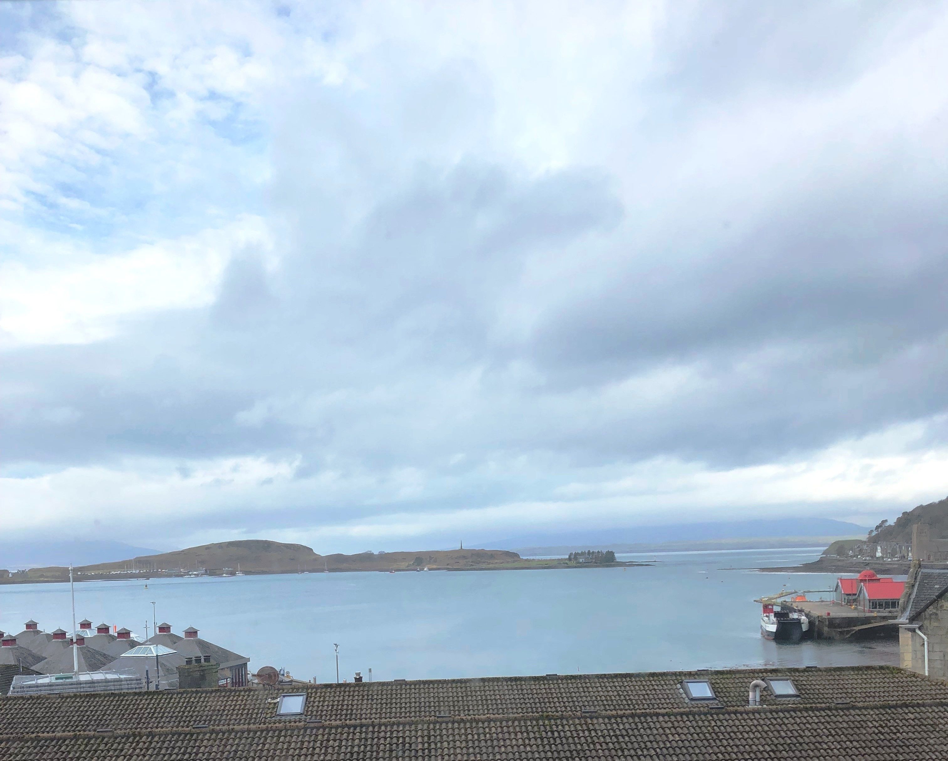 A coastal view with a calm sea, a hilly landscape, and a small harbor with boats.