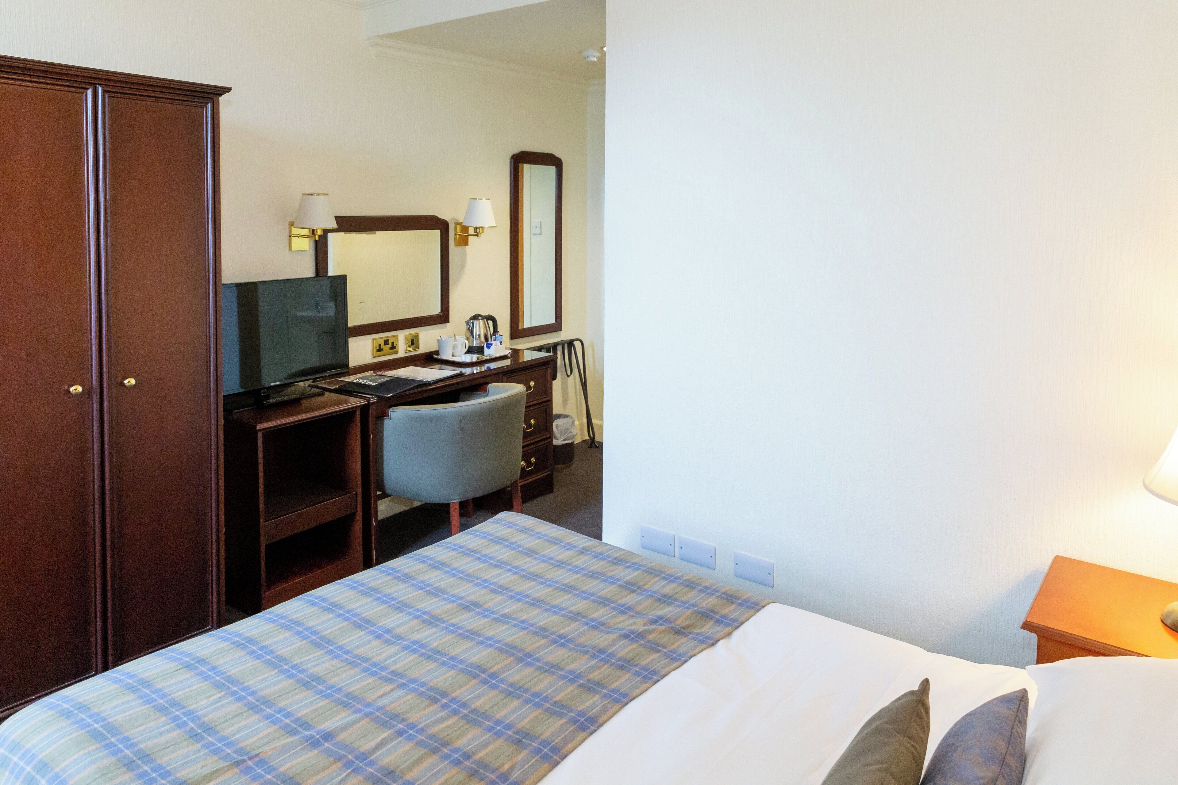A hotel room with a bed, a desk, a chair, a wardrobe, and a mirror.