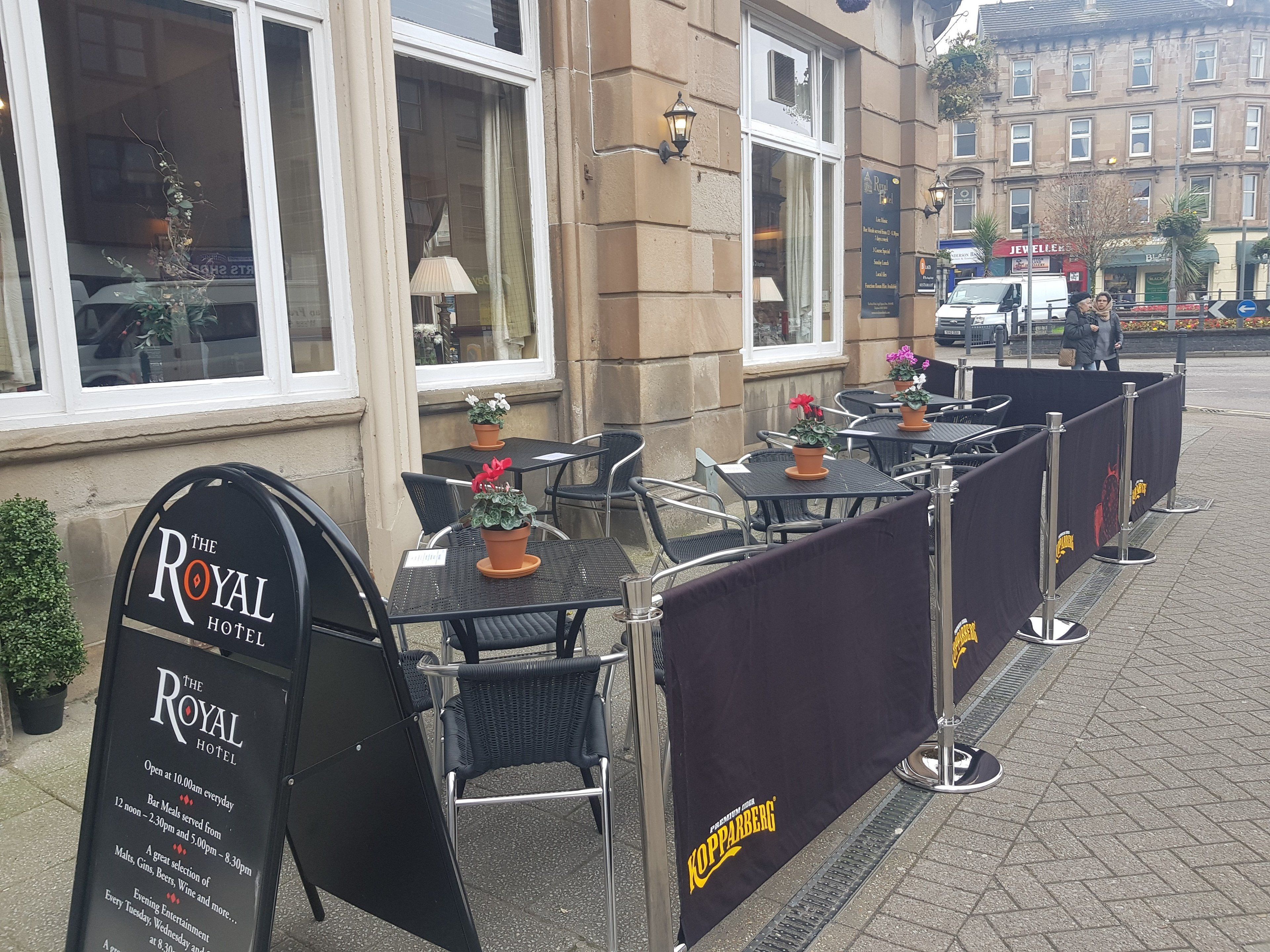 Outdoor seating with tables and chairs, a sign for The Royal Hotel, and a Koppaberg banner.