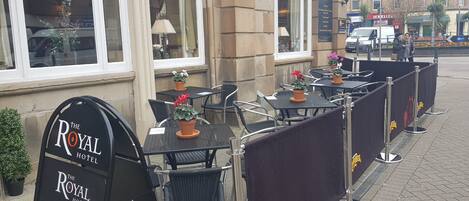 Outdoor seating with tables and chairs, a sign for The Royal Hotel, and a Koppaberg banner.