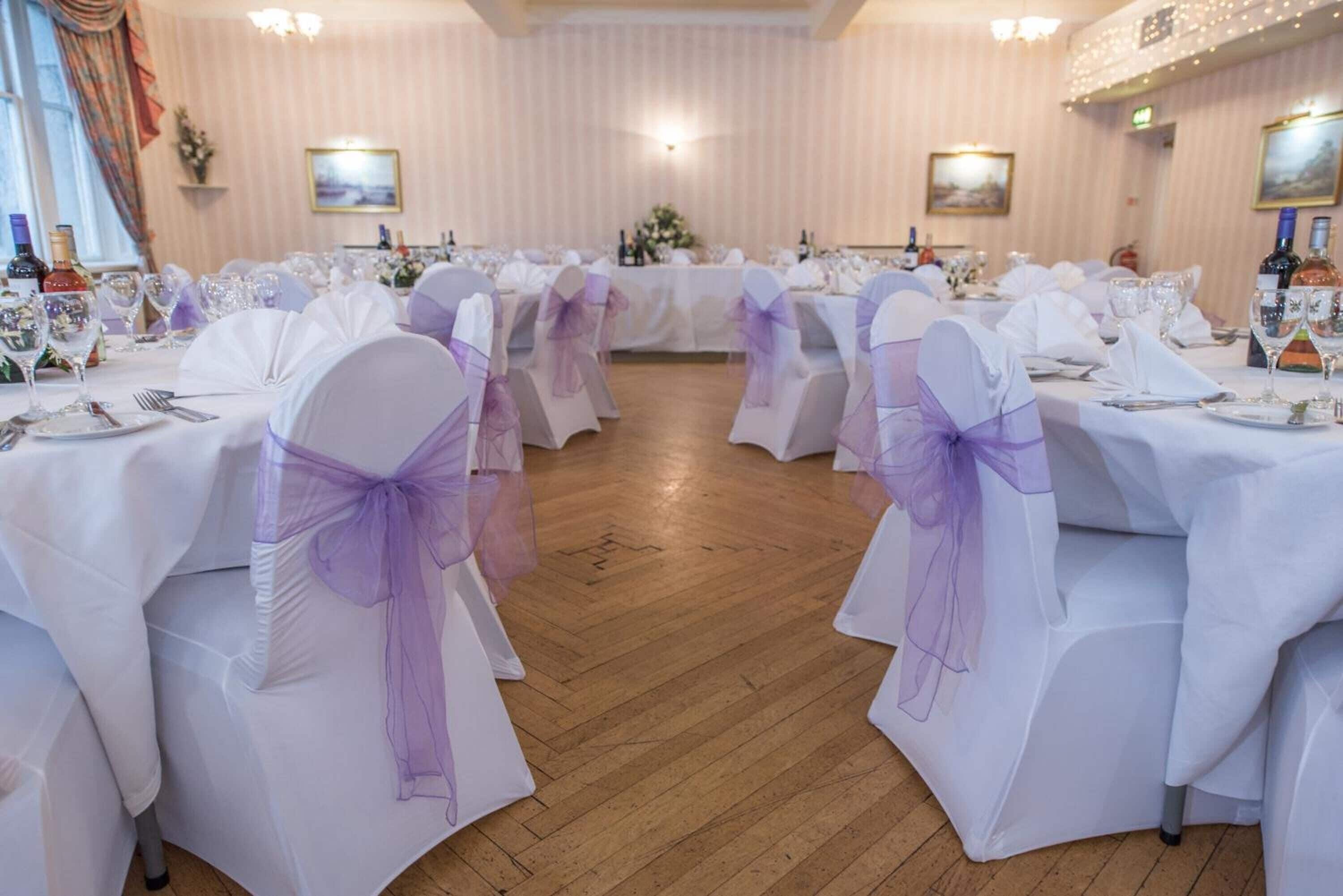 A banquet hall with round tables set for a formal event, featuring white tablecloths and purple sashes.