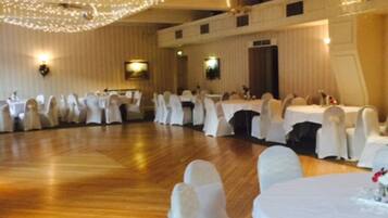 A banquet hall with round tables covered in white tablecloths, white chairs with sashes, and string lights on the ceiling.