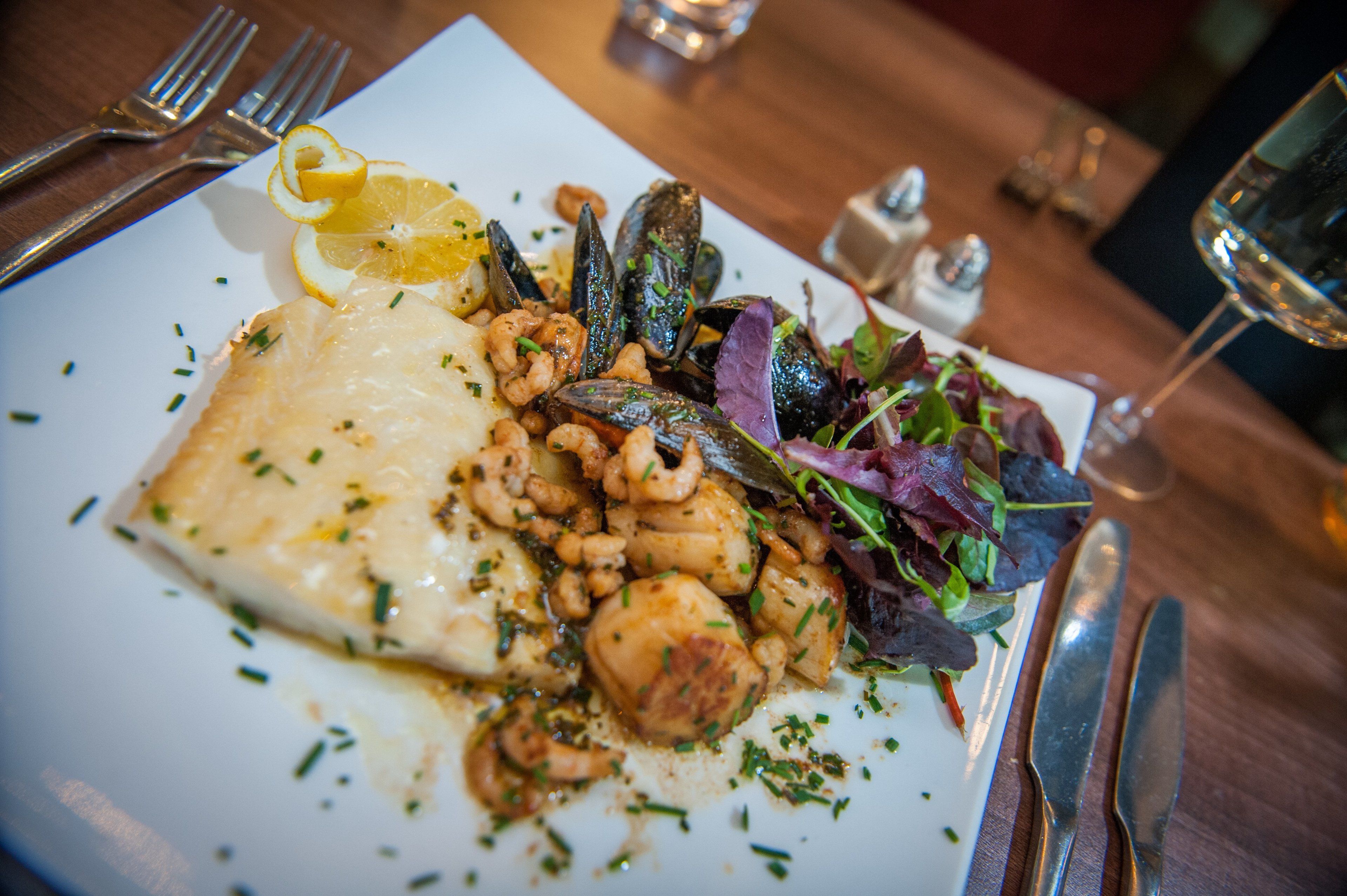 Un plat de menjar amb una varietat d'ingredients, incloent marisc i verdures, sobre un plat blanc.