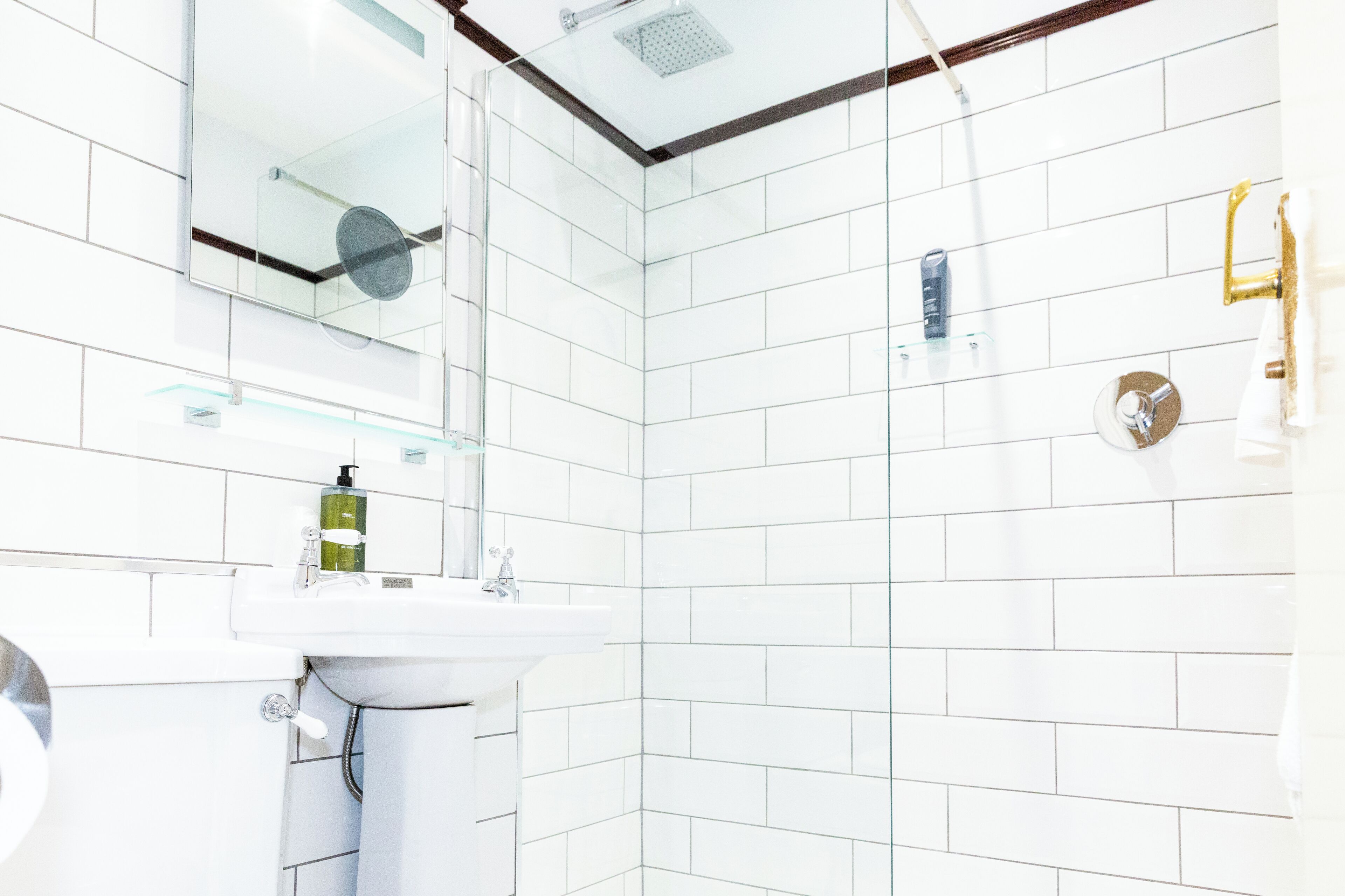 A modern bathroom with white tiles, a glass shower enclosure, and a sink with a soap dispenser.
