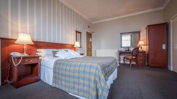 A hotel room with a bed, bedside lamps, a desk with a chair, and a wardrobe.