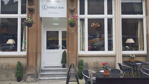 A building with a sign for 'Strathmore Hotels Lounge Bar @ The Royal'. There are steps leading to the entrance, a small potted plant on the steps, and a chair and table outside. - The Royal Hotel (Oban)