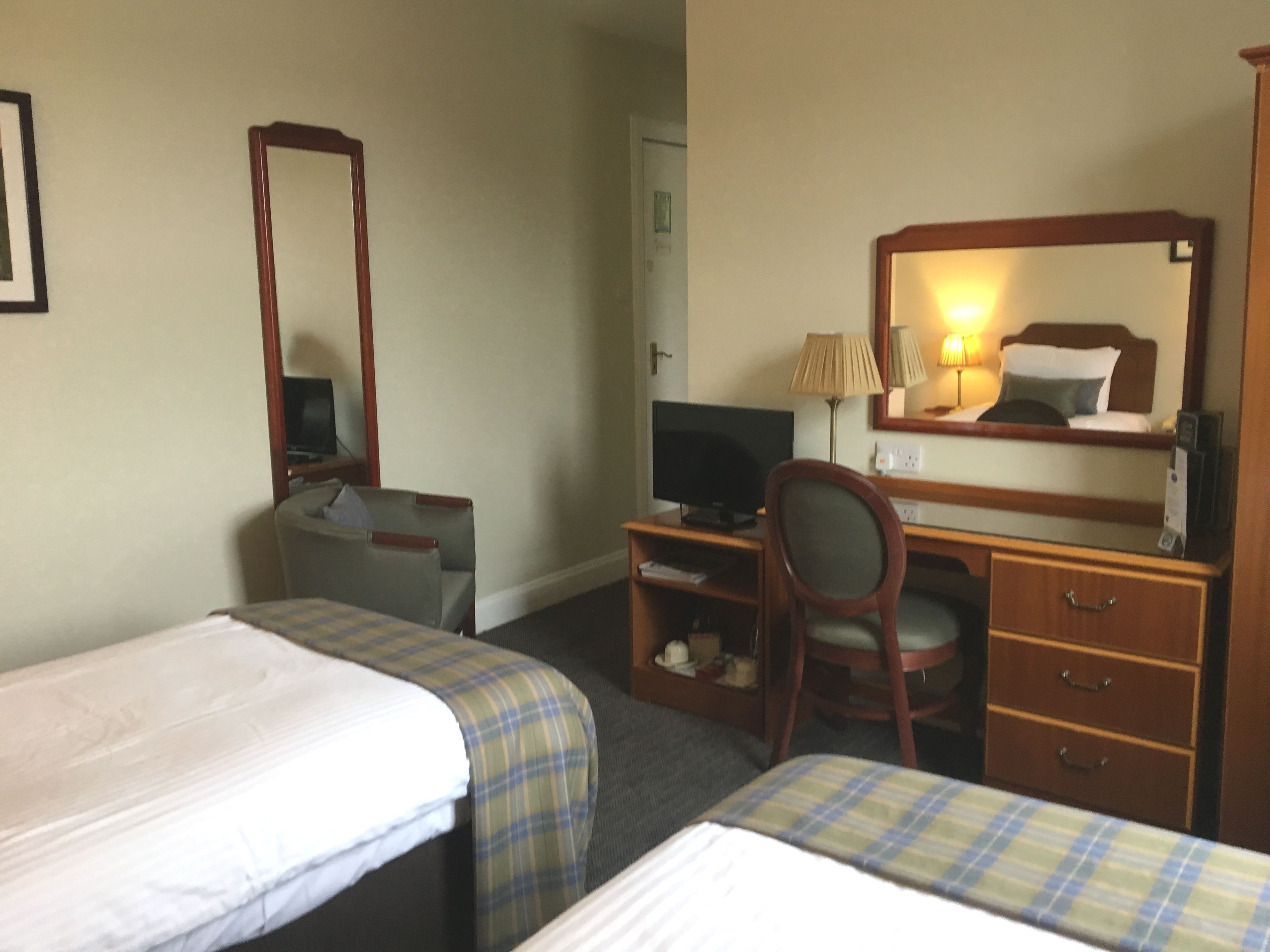 Ett hotellrum med två separata sängar, ett skrivbord med en dator, en stol, en TV och en garderob.