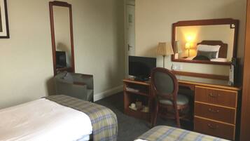 A hotel room with two single beds, a desk with a computer, a chair, a TV, and a wardrobe.
