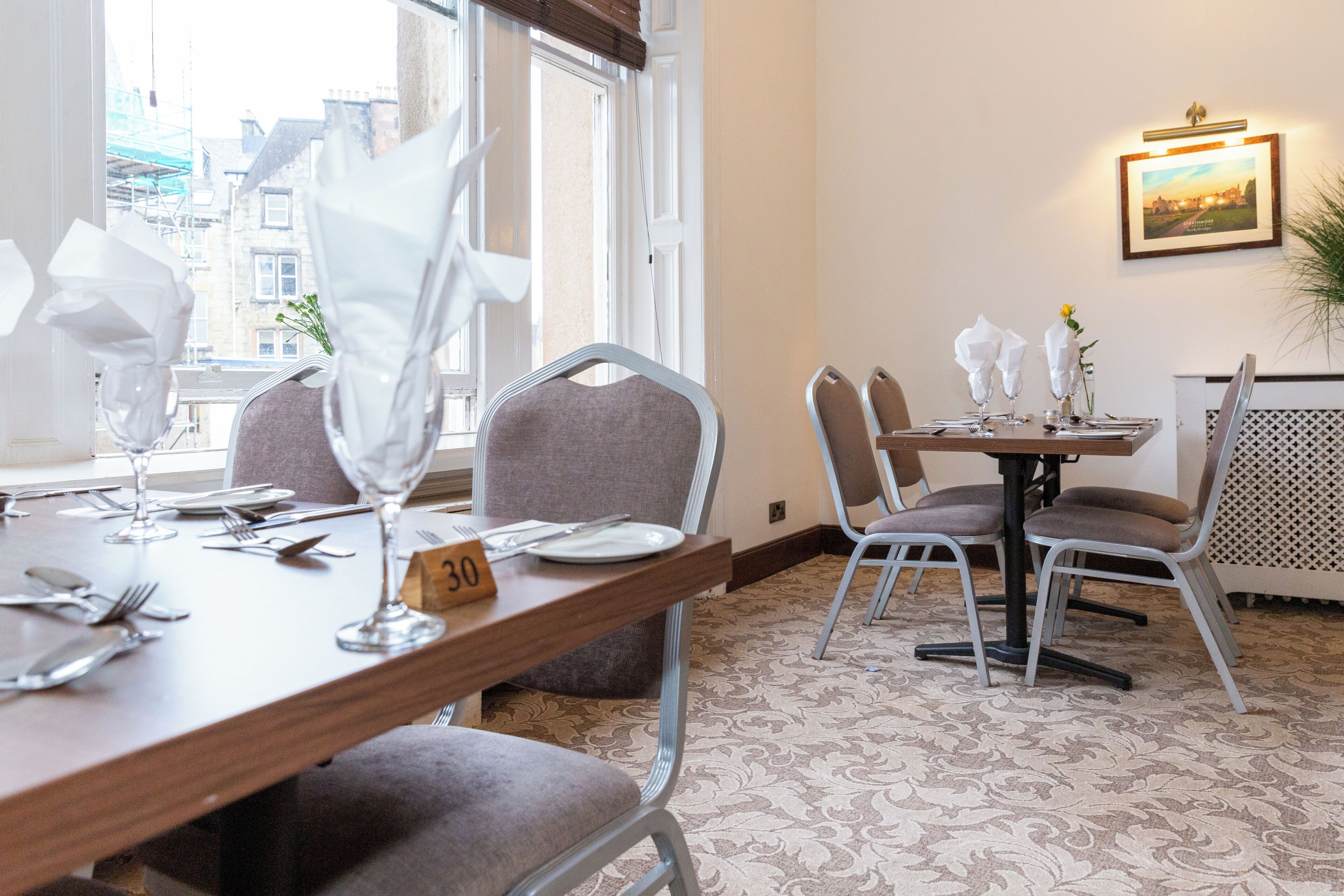 A dining area with tables set for four, numbered 30, and chairs with cushioned seats.