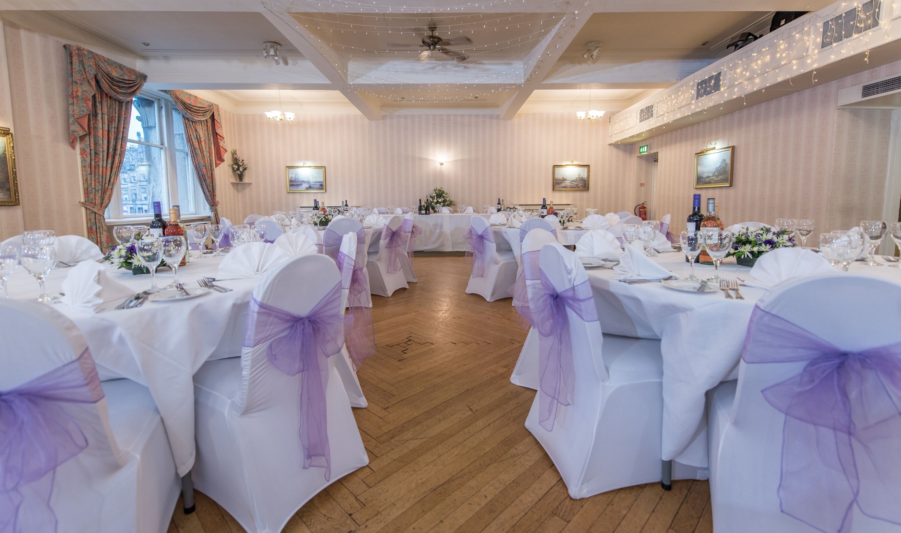 A banquet hall with round tables, white tablecloths, and purple sashes.