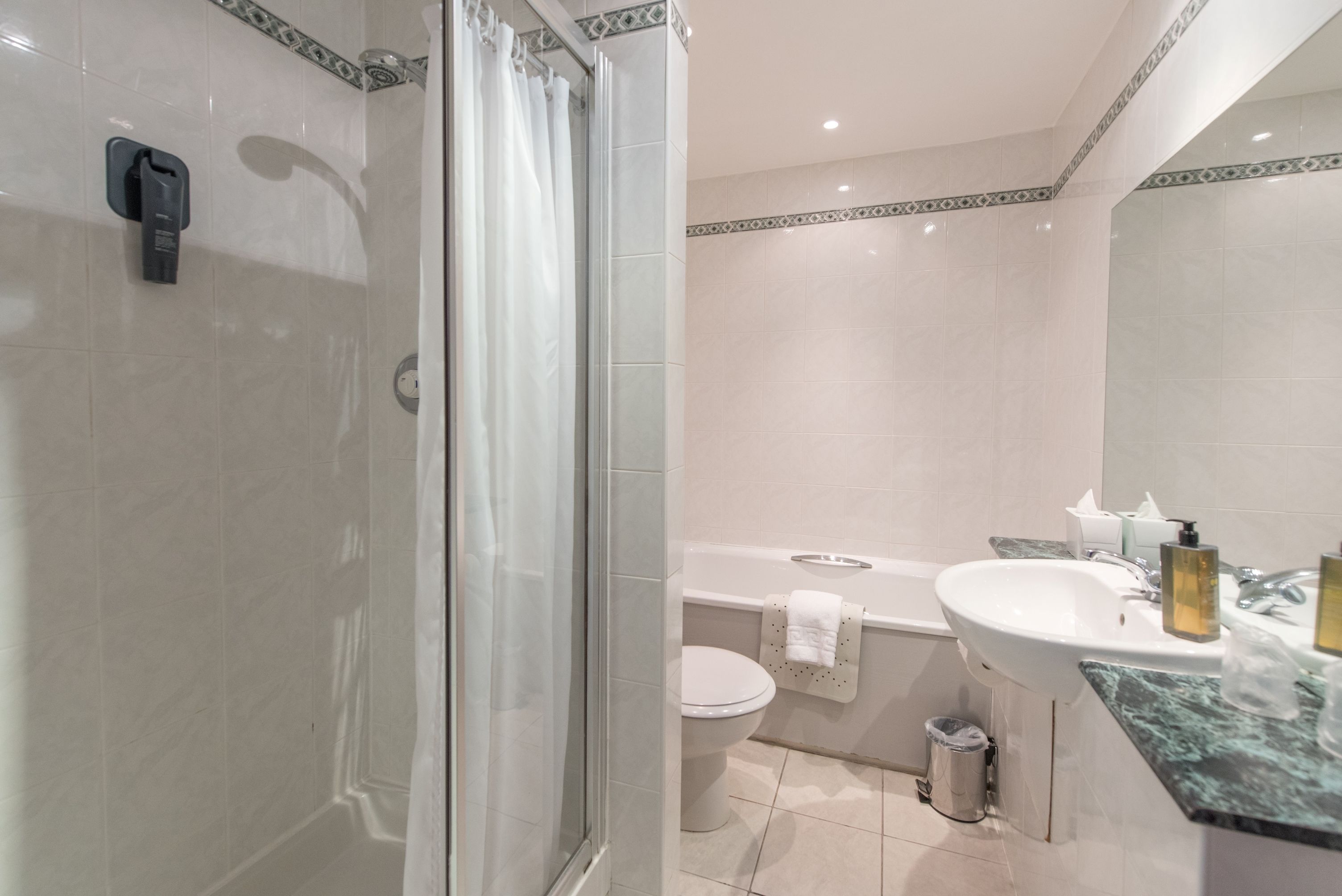 A modern bathroom with a glass-enclosed shower, a white toilet, a bathtub, and a sink with a marble countertop.