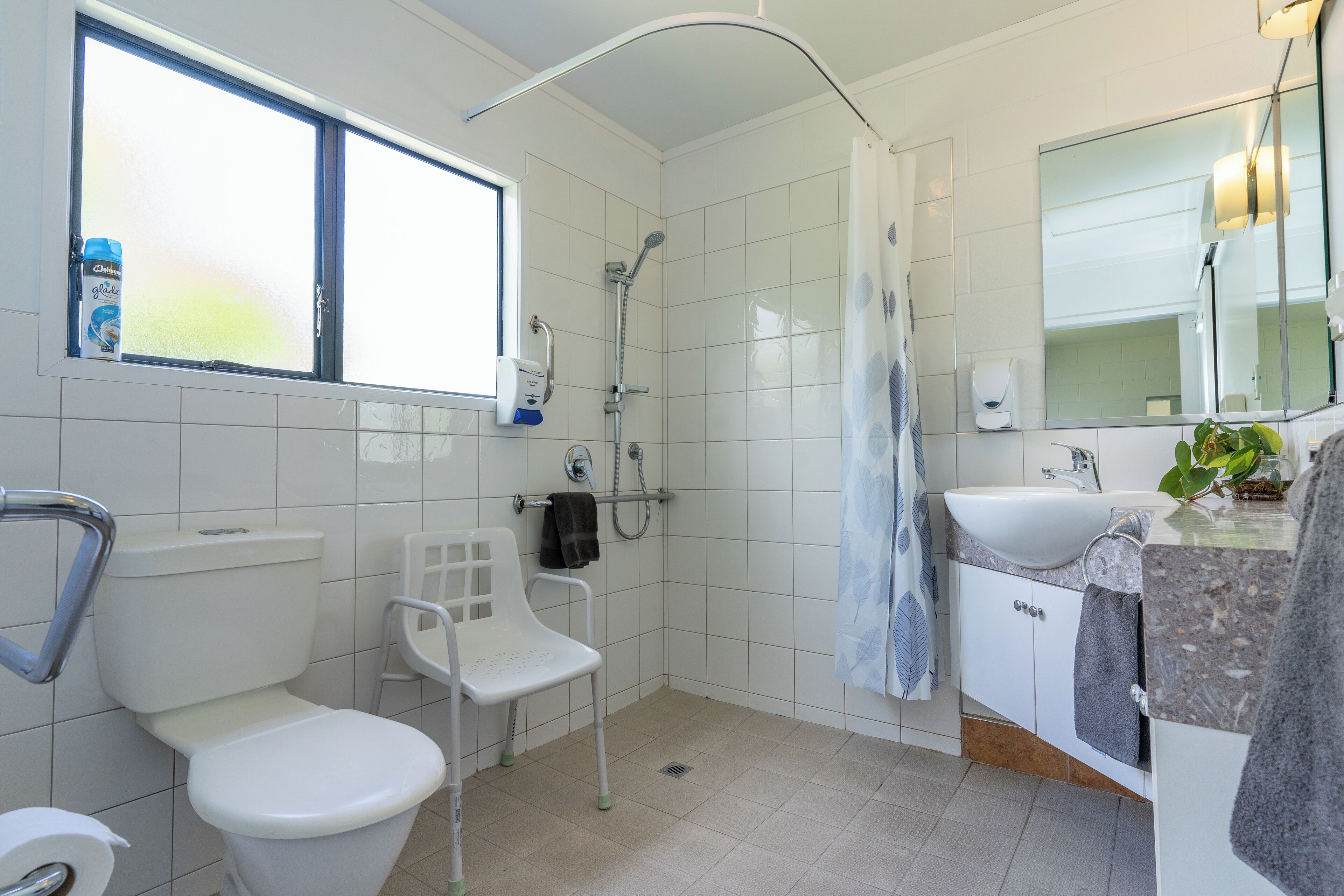 Een moderne badkamer met toilet, douche, wastafel en een stoel.