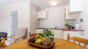A dining area with a wooden table set with fruits, a chair, and a small potted plant. - Loredo Motel (Kaitaia)