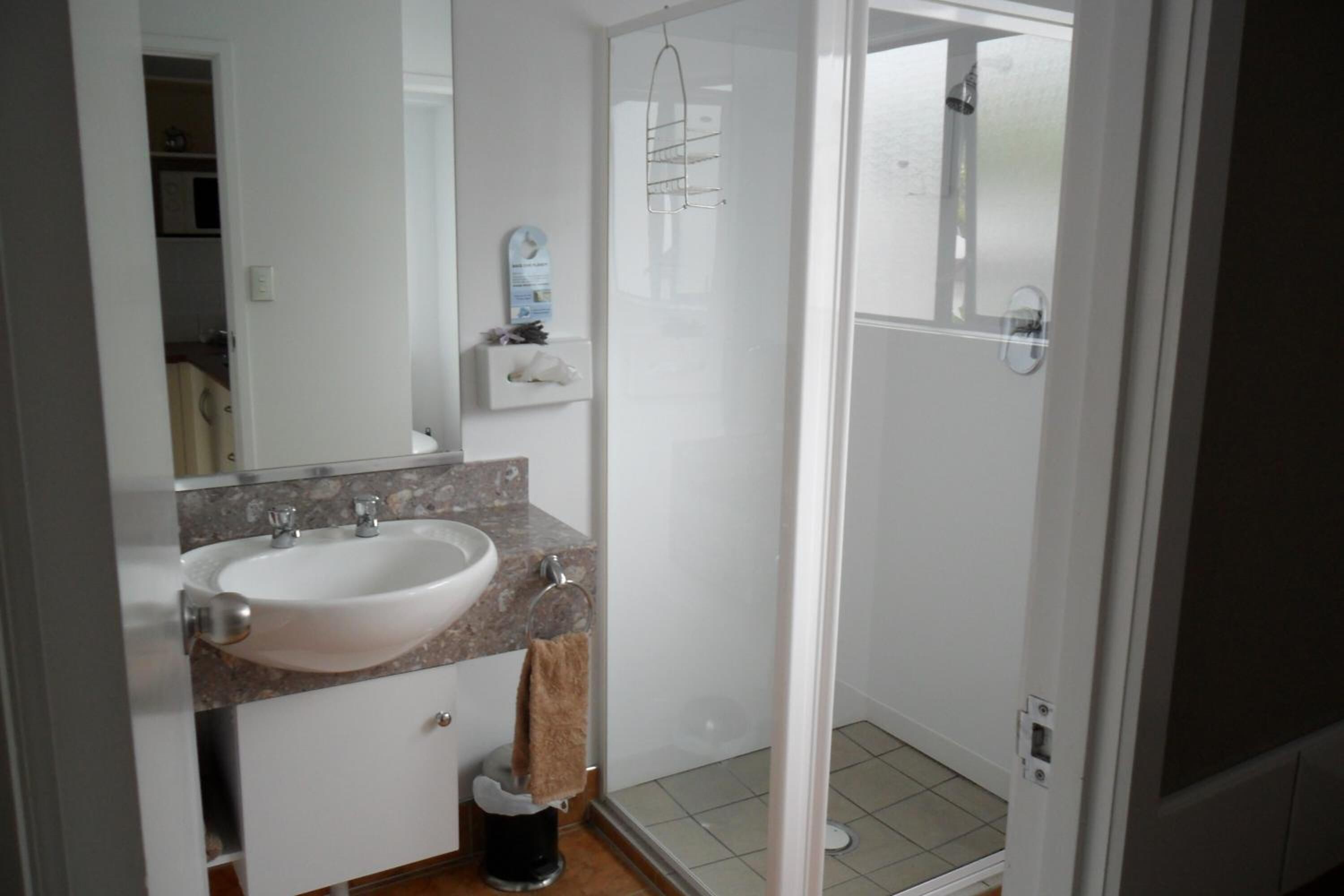 A bathroom with a white sink, a mirror, a towel rack, and a glass shower enclosure.