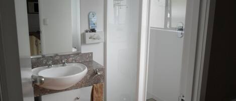 A bathroom with a white sink, a mirror, a towel rack, and a glass shower enclosure.