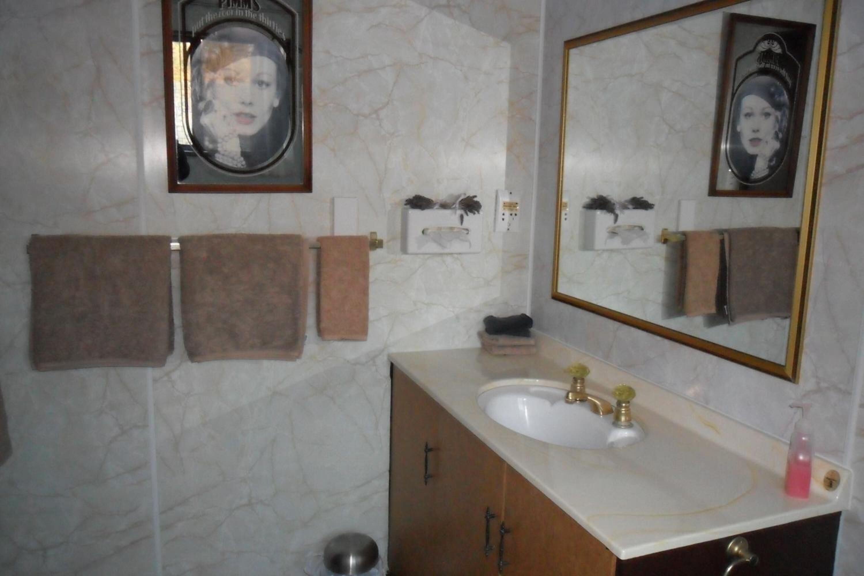 A bathroom with a marble wall, a sink with a gold faucet, and a large mirror. There are three towels hanging on the wall.
