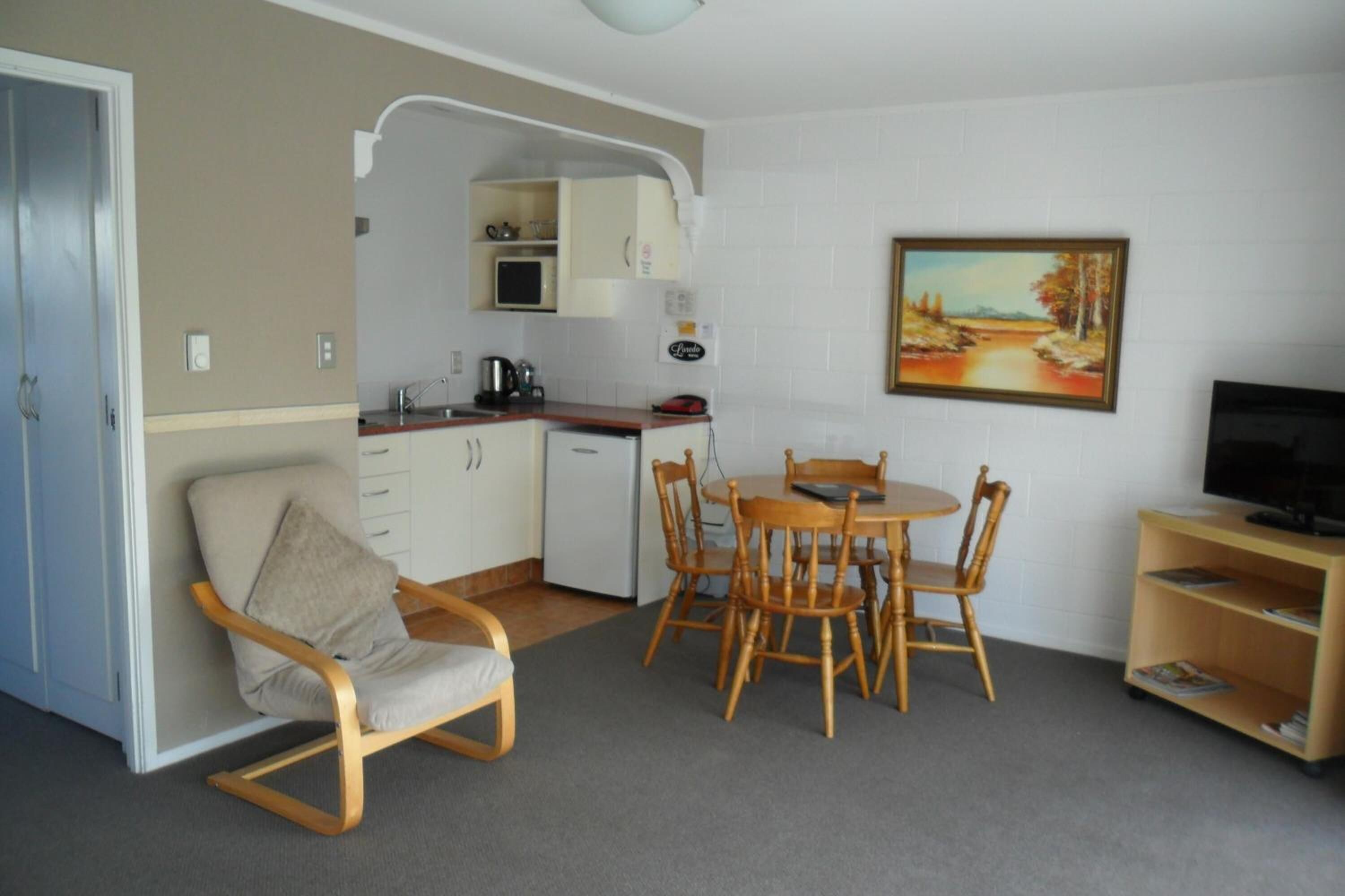 A compact living space with a kitchenette, dining area, and a TV on a shelf.