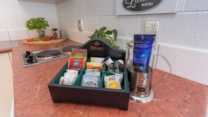 A kitchen counter with a coffee maker, a box of coffee pods, and a coffee mug. - Loredo Motel (Kaitaia)
