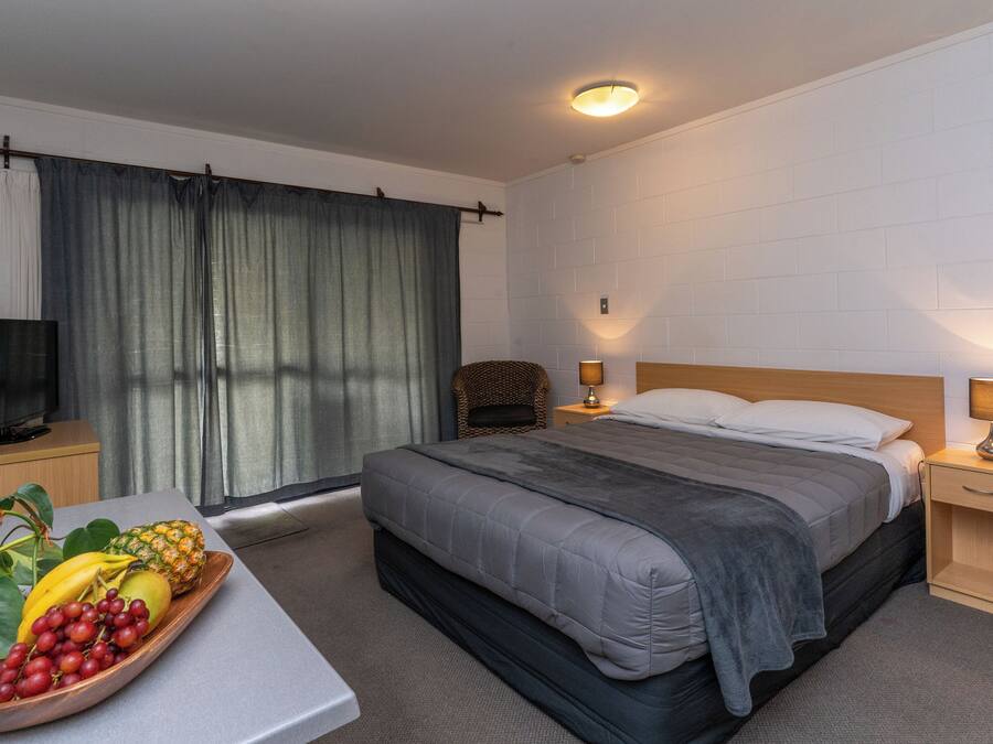 A hotel room with a bed, bedside lamps, a television on a nightstand, and a fruit tray on the table.